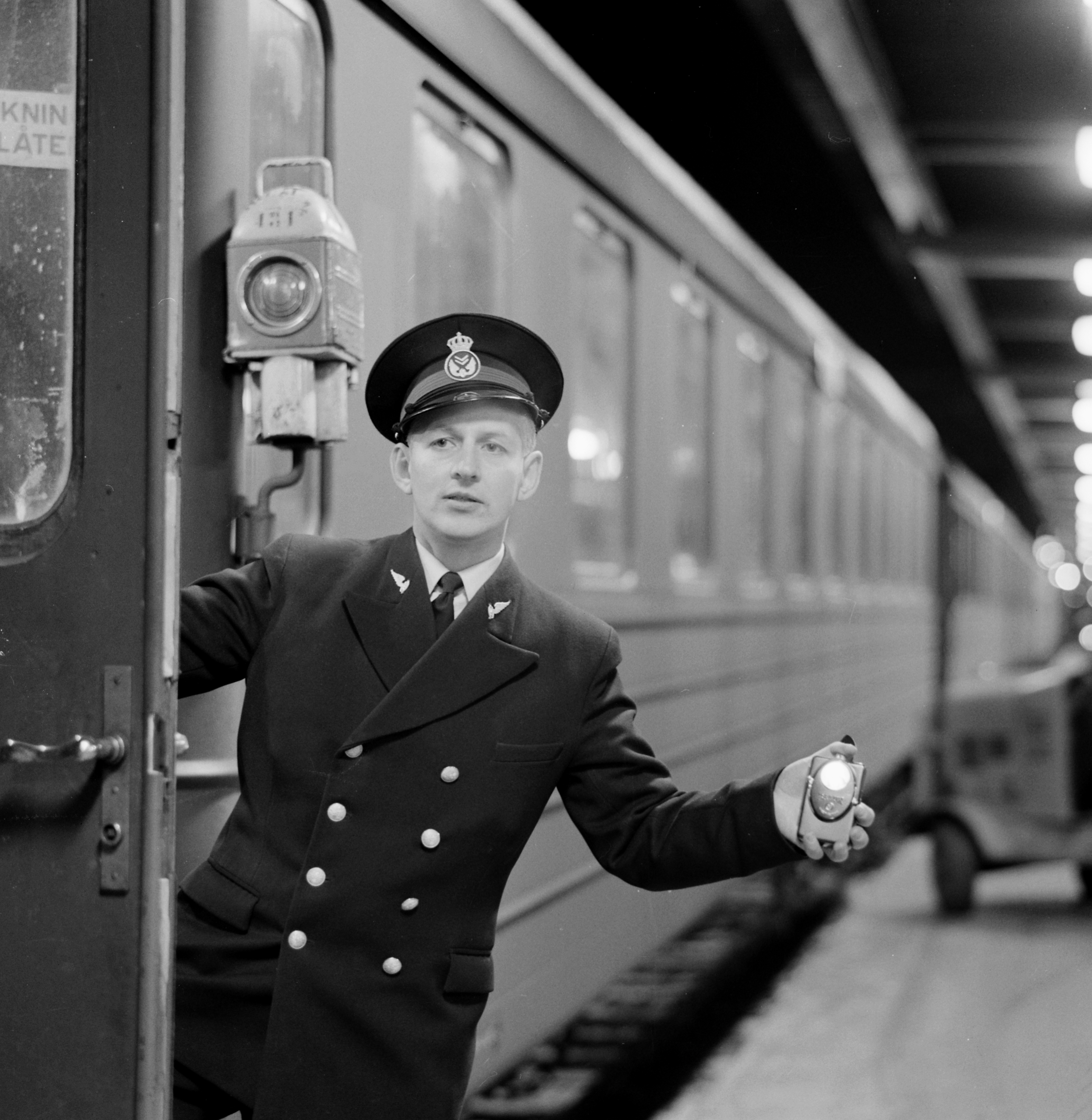 Uniformed conductor hanging out through an open door and giving a signal.