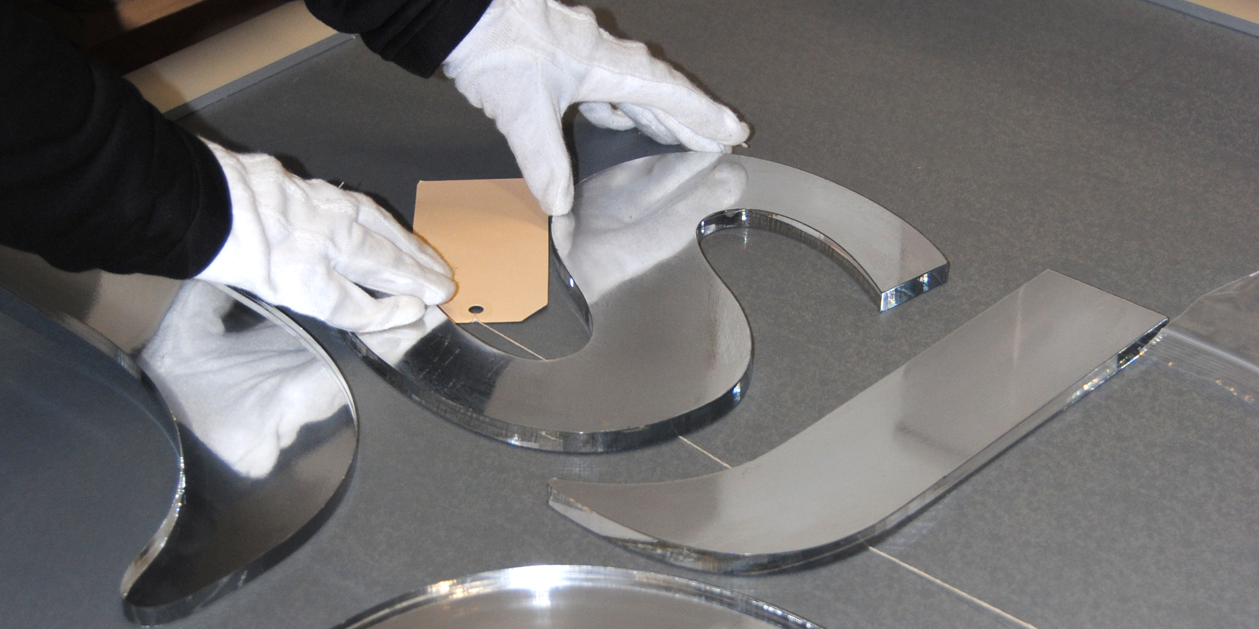 Two hands wearing white gloves prepares a silver SJ sign to be archived.