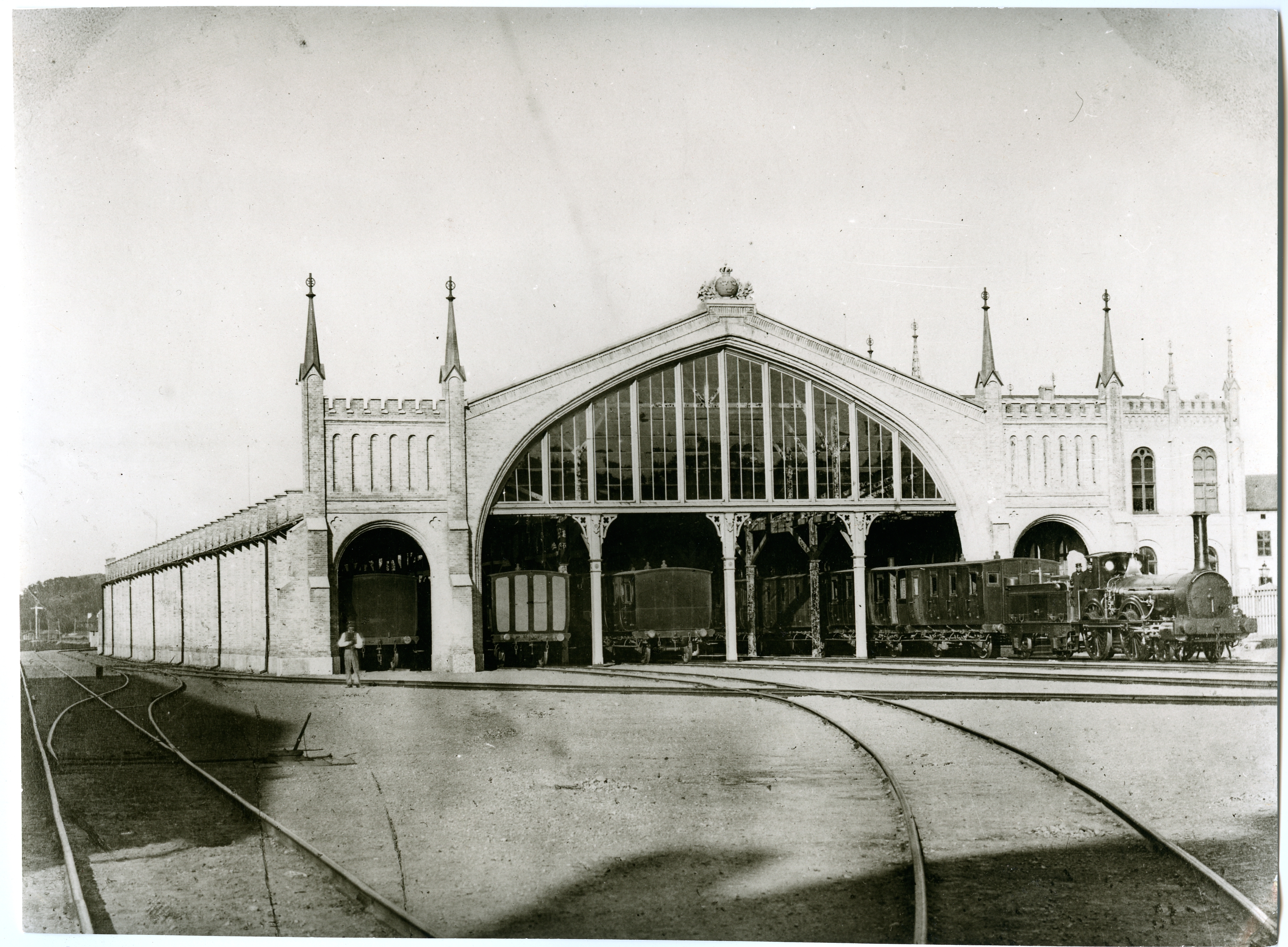 Magnificent train hall from the front with locomotives and wagons parked on tracks that go towards the camera.