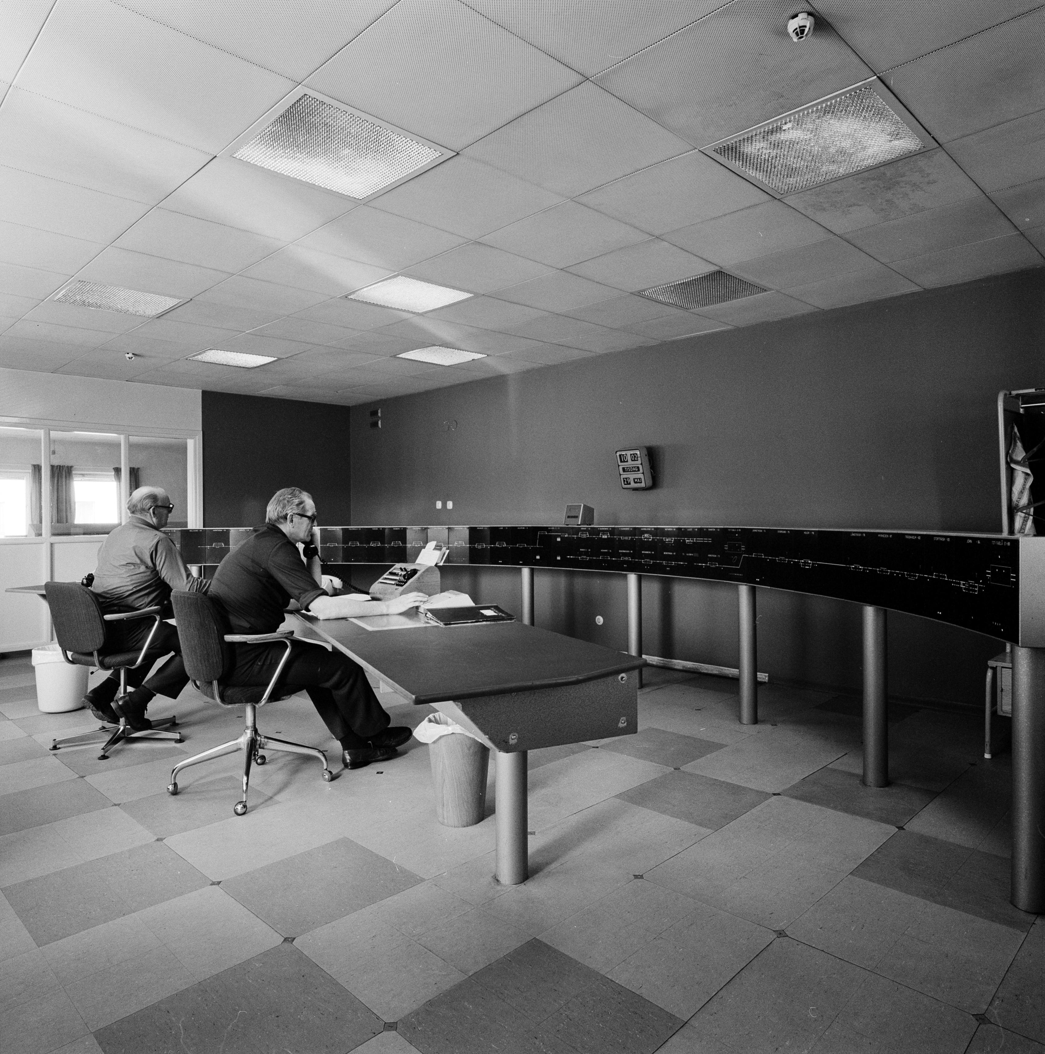 A sterile control room with two men in office clothes sitting at a large table and working over the phone.