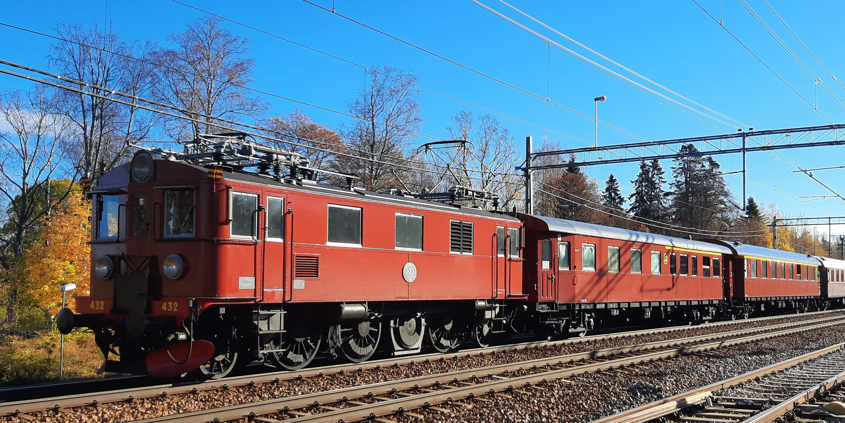 Rött lok med röda vagnar på räls i höstlandskap.
