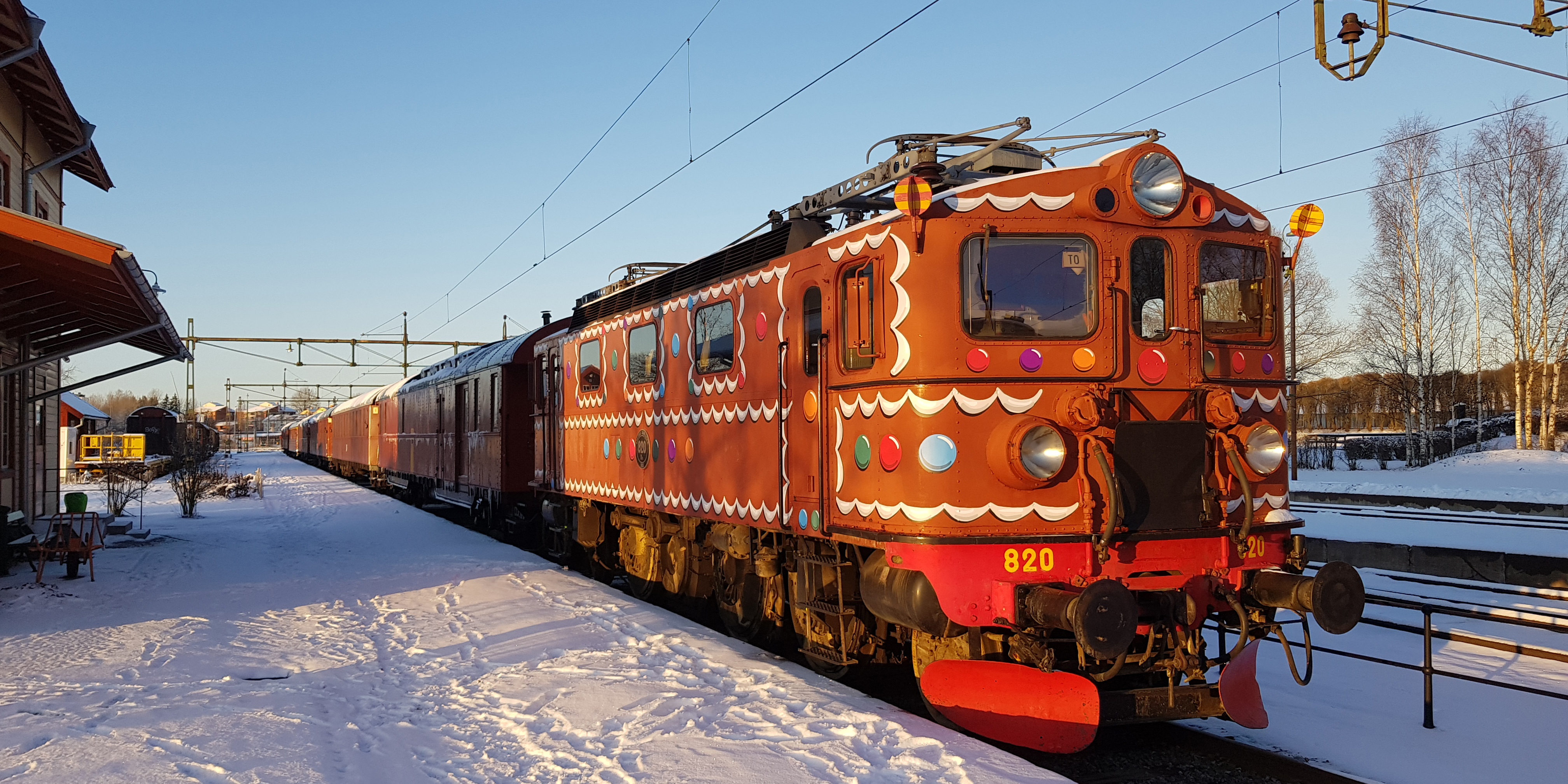 Utsmyckat lok med vagnar framför station i vintrigt landskap.