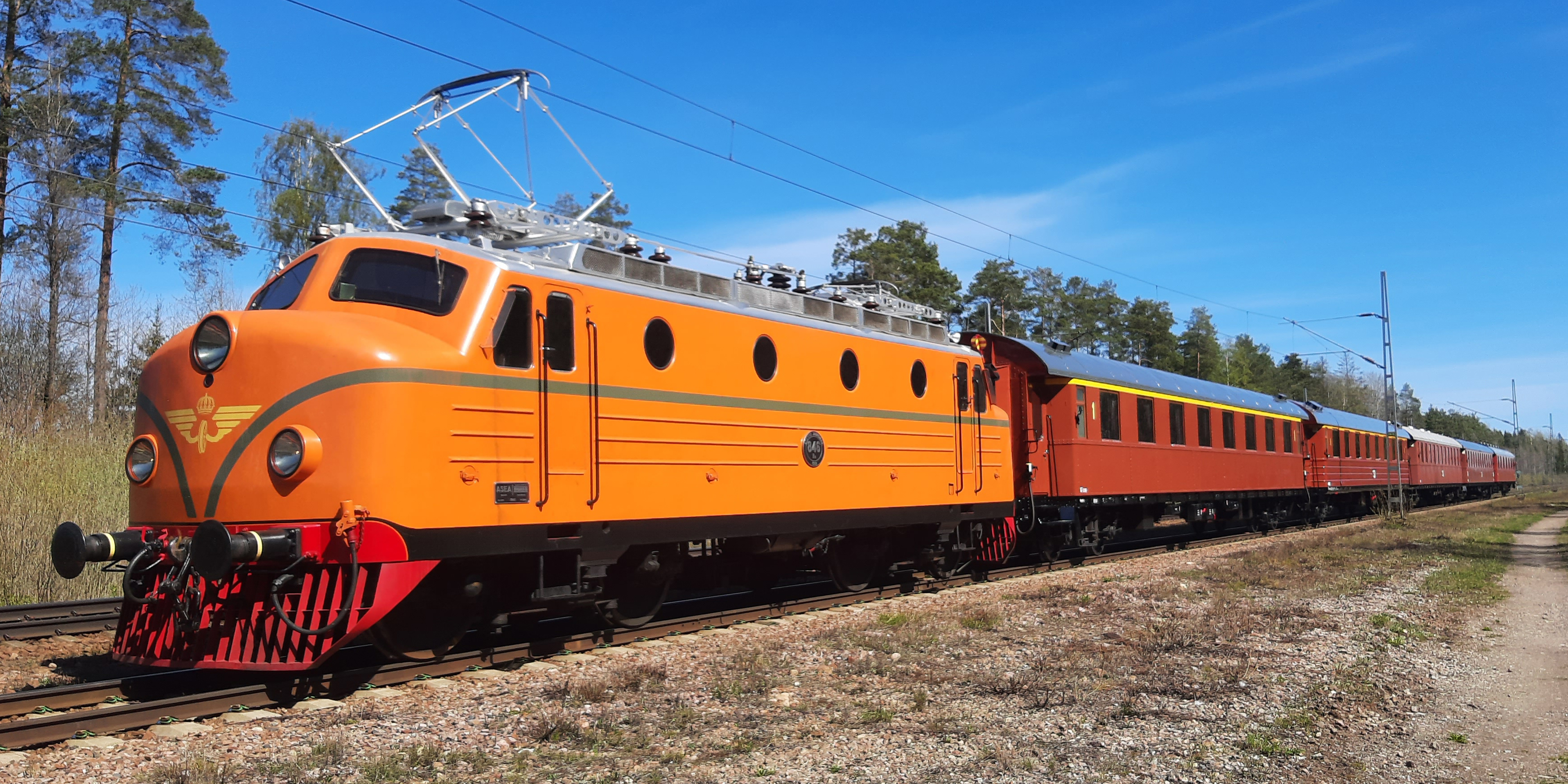 Orange lok med flera personvagnar står framför en sommargrön skog.