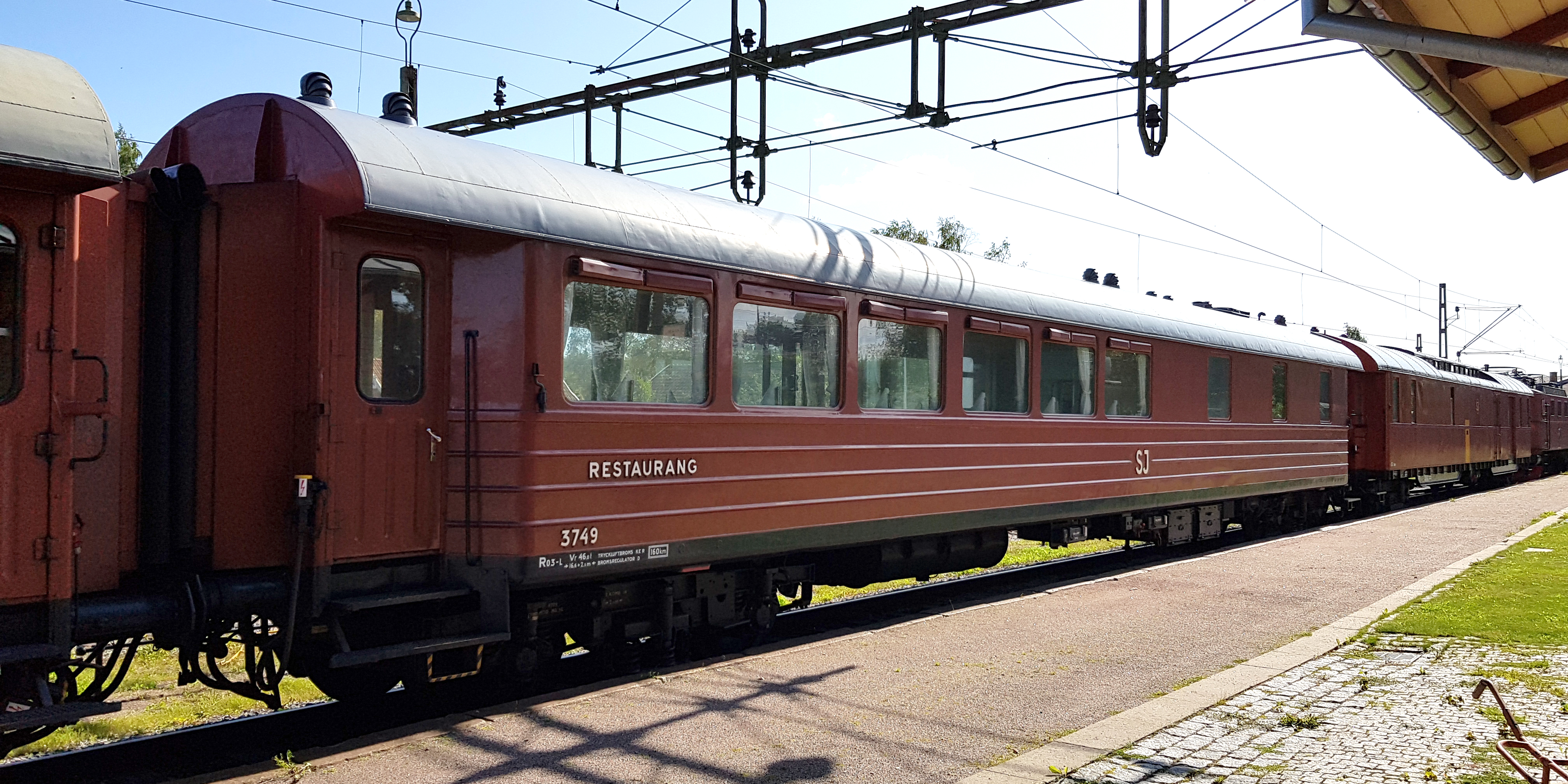 Roströd personvagn kopplad mellan andra vagnar vid perrong.