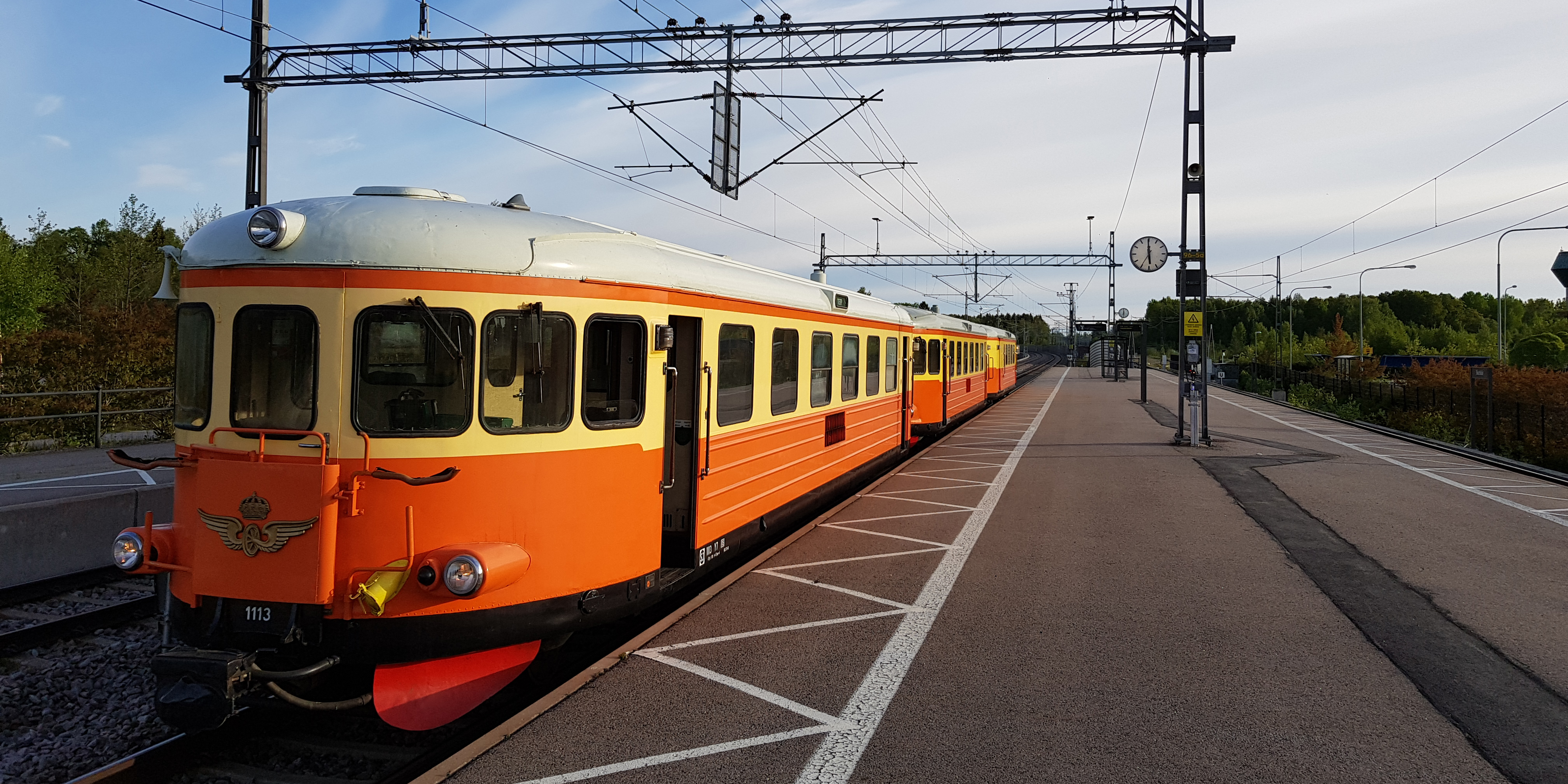 Orange-gul rälsbuss med flera vagnar parkerad vid perrong.