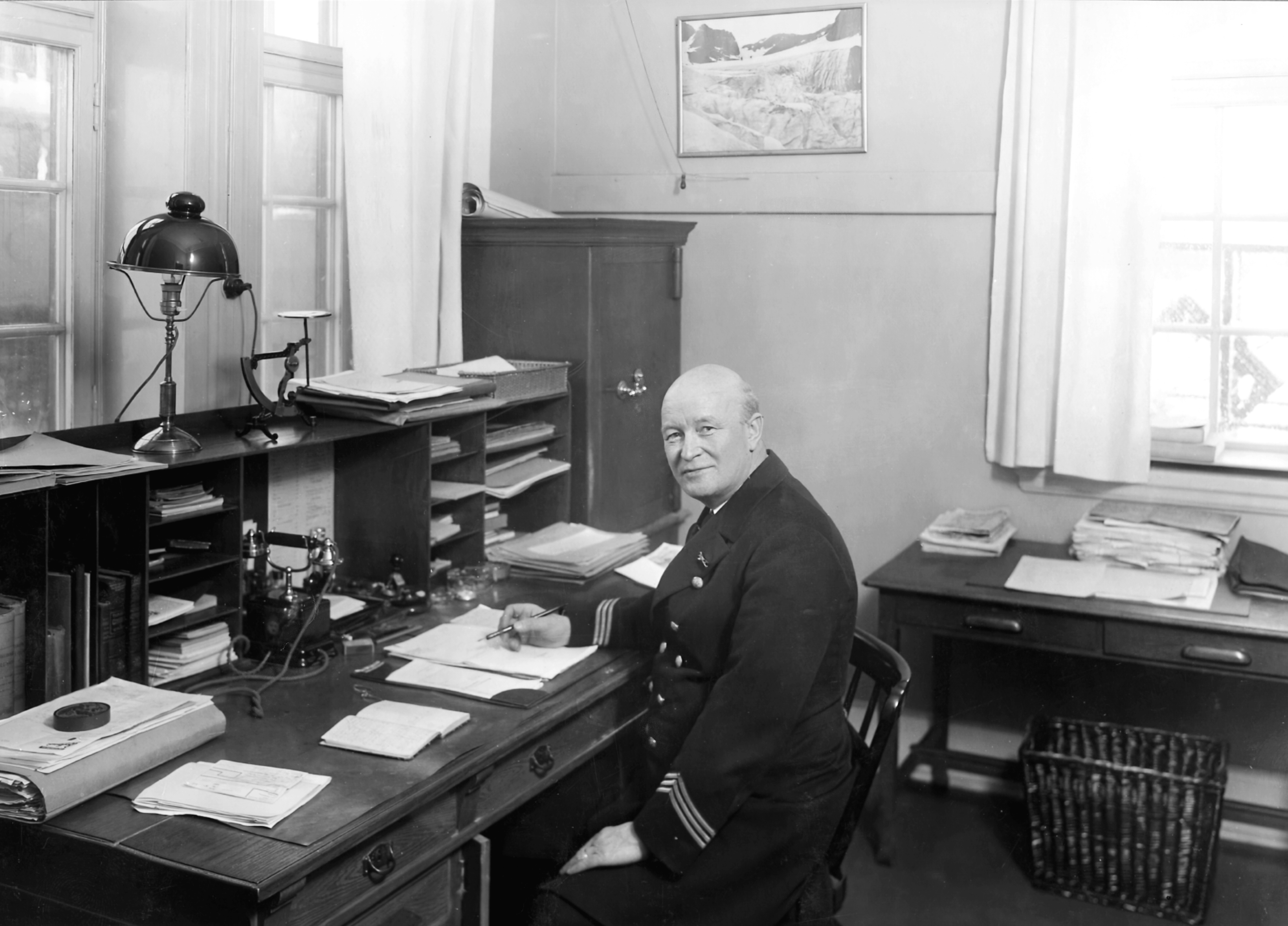 A man in uniform sitting at a stylish and well-arranged desk, looking into the camera.