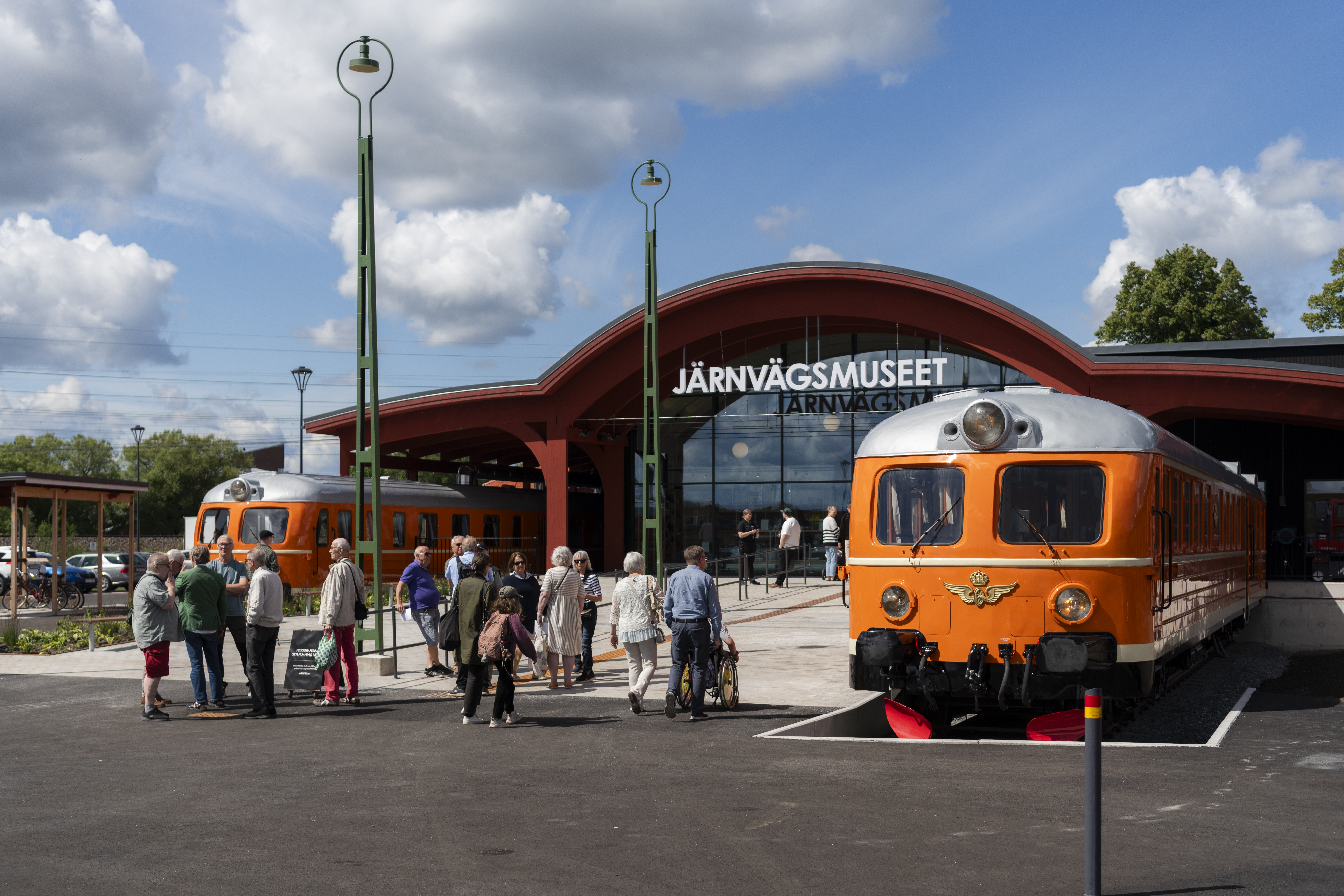 entren till järnvägsmuseet, det syns två orangea tåg som ramar in huvudingången. Utanför står en grupp människor påväg in.