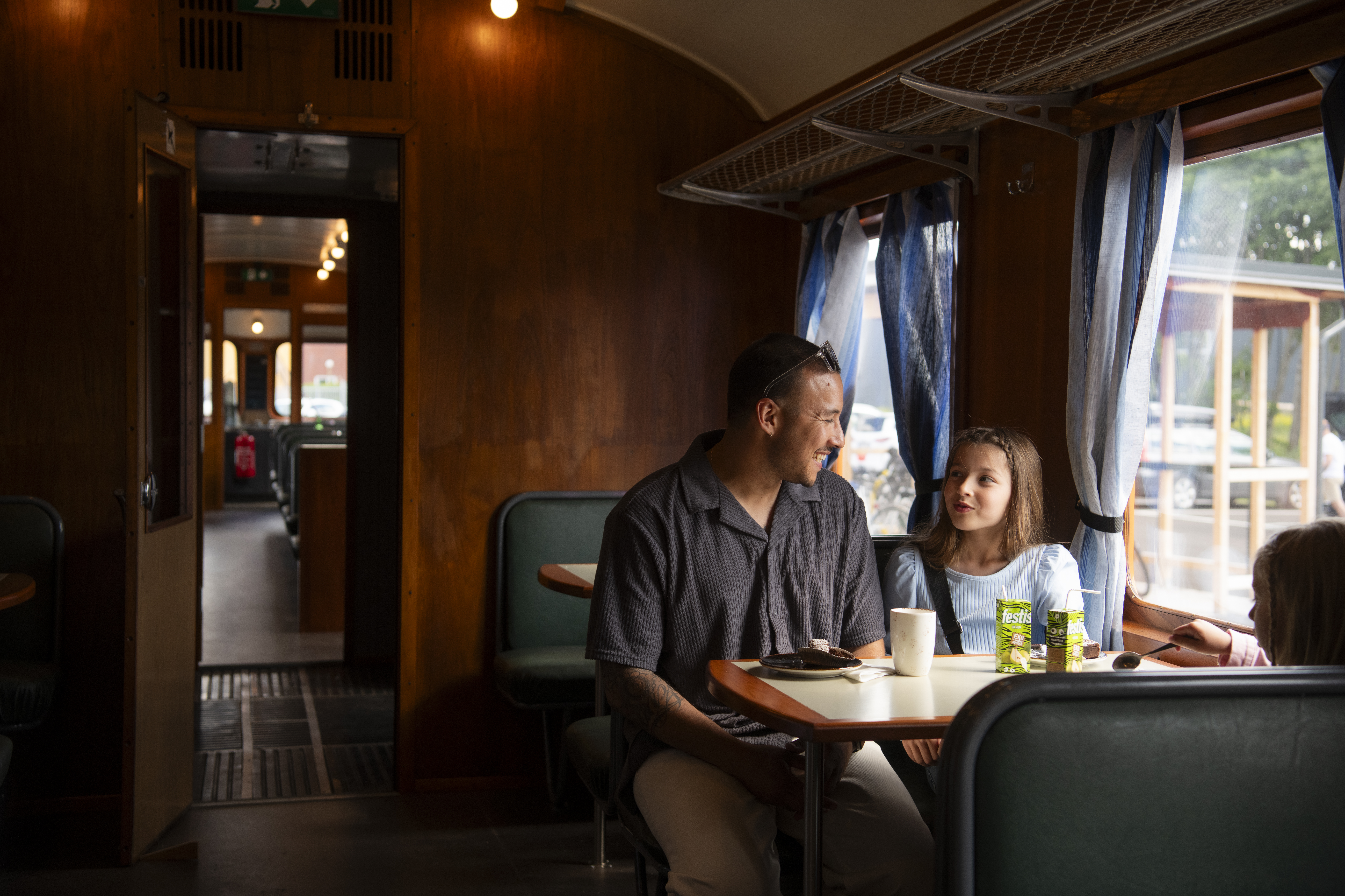 A father and his child are having a snack in a stationary train carriage.