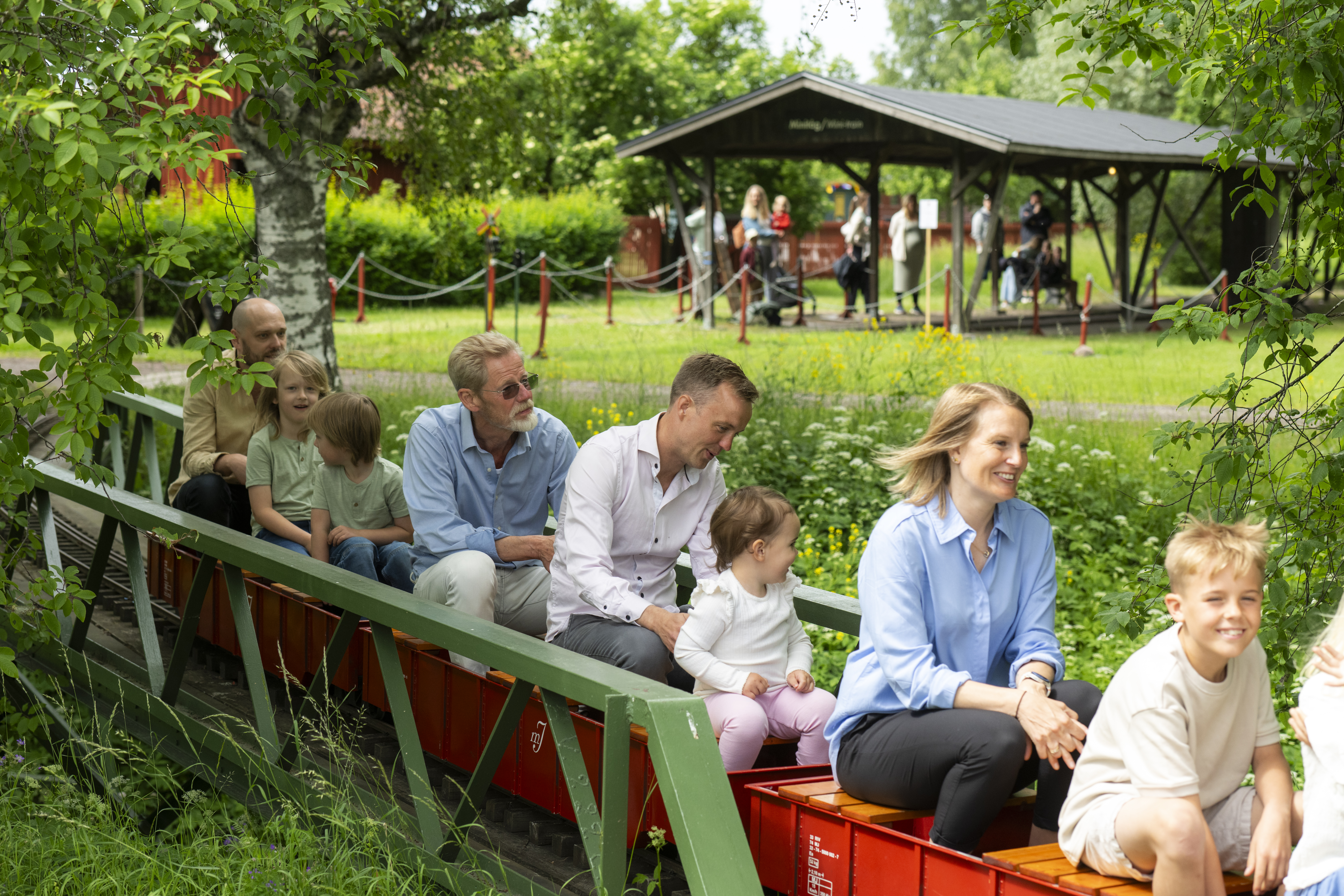 Children and adults ride on a miniature train through the green countryside.