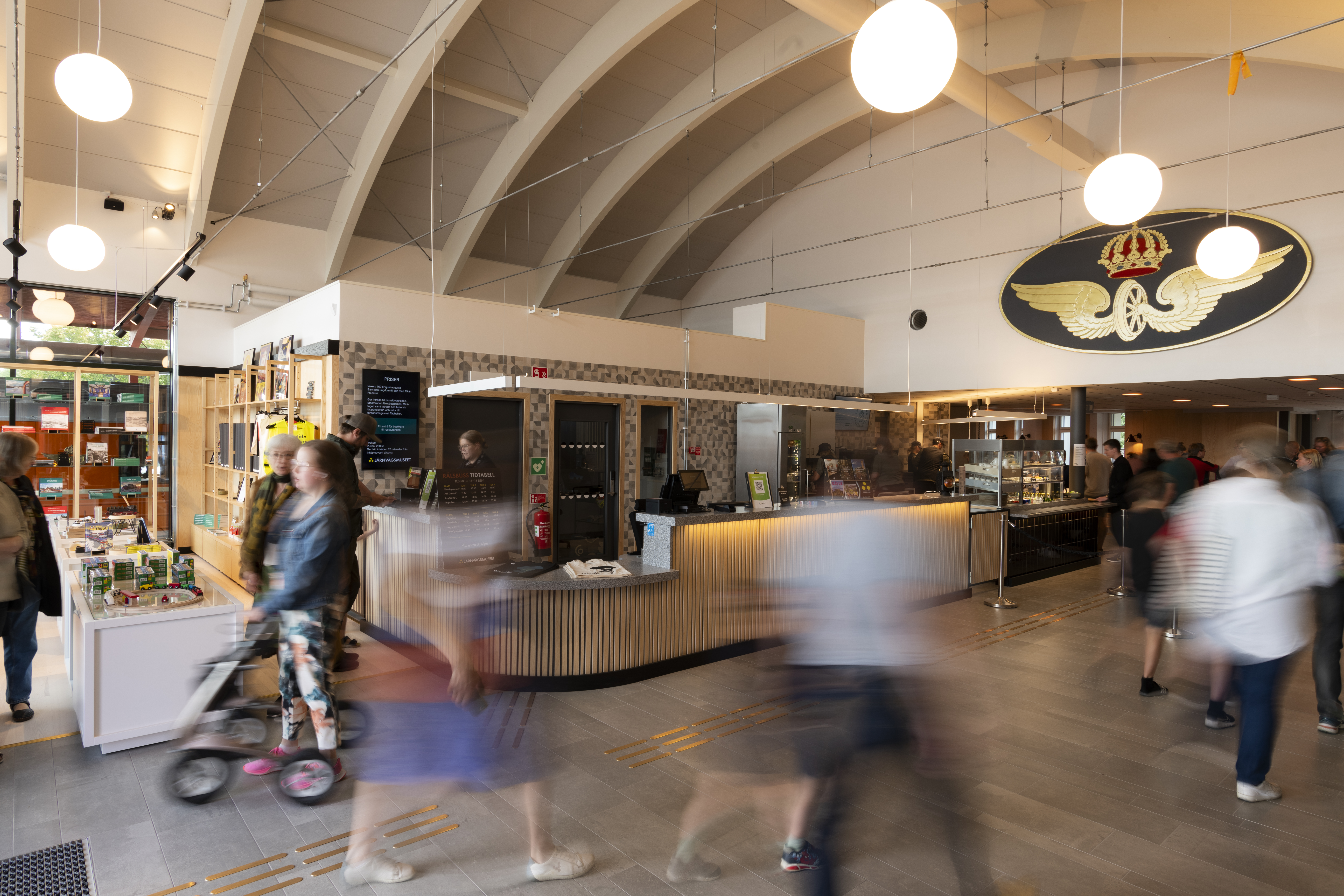 Flera människor är i rörelse i museets entré. Museibutiken med ljusa trähyllor och fina föremål syns i bakgrunden.