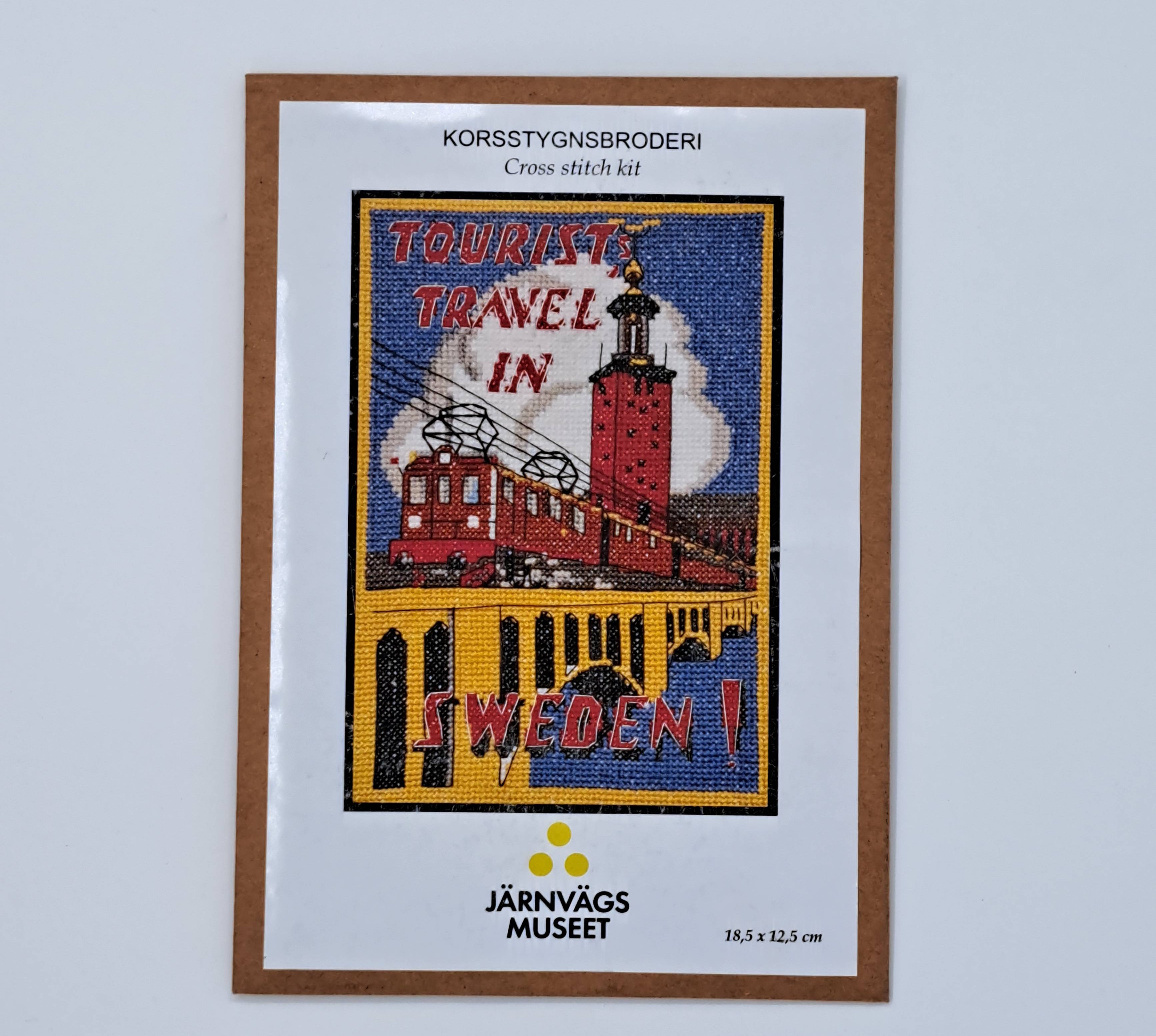 Ett broderikit med motiv av ett tåg i Stockholmsmiljö och texten "Tourist travel in Sweden"