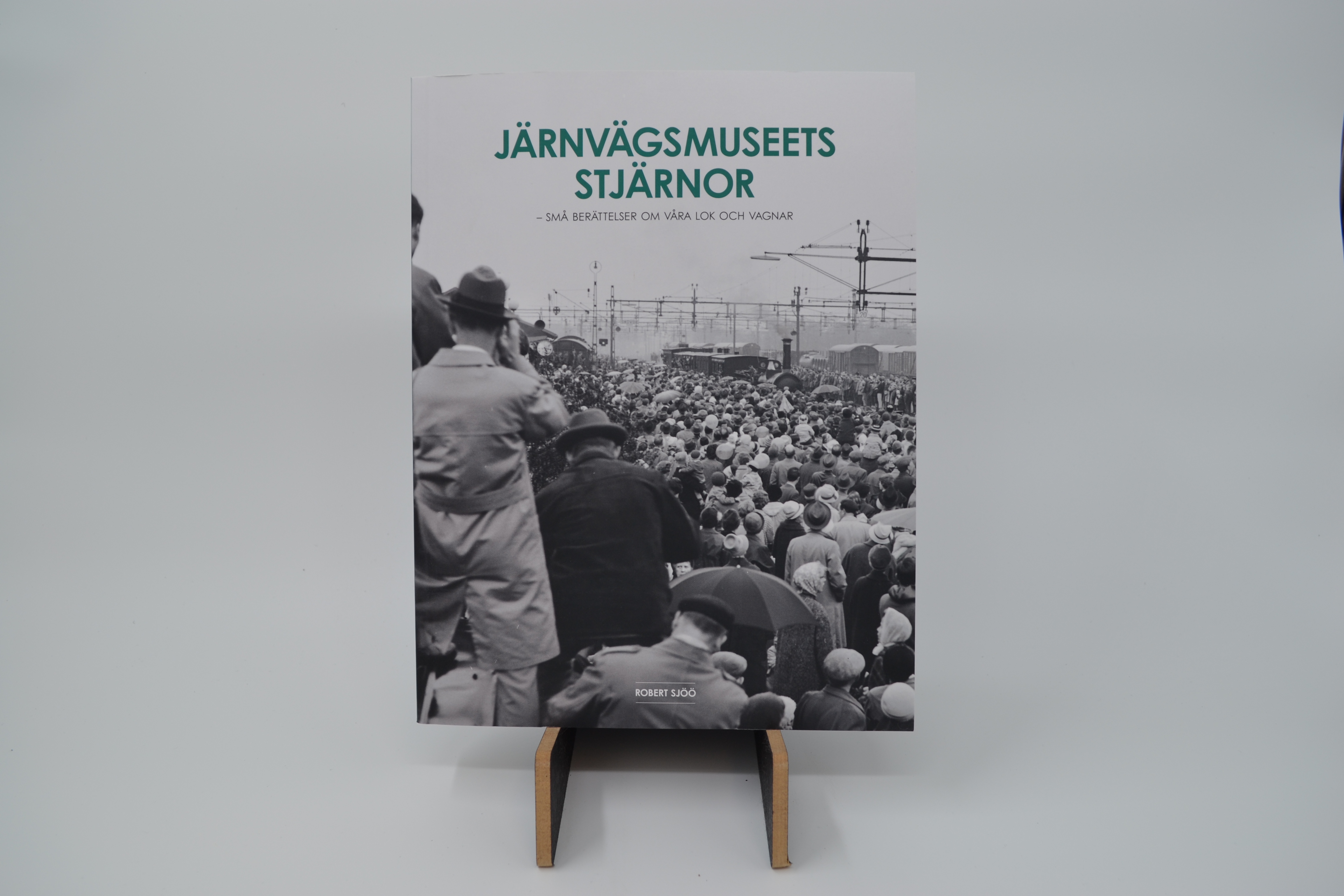 Det svartvita omslaget till boken "Järnvägsmuseets stjärnor" pryds av en folkhop som står och tittar efter ett tåg.