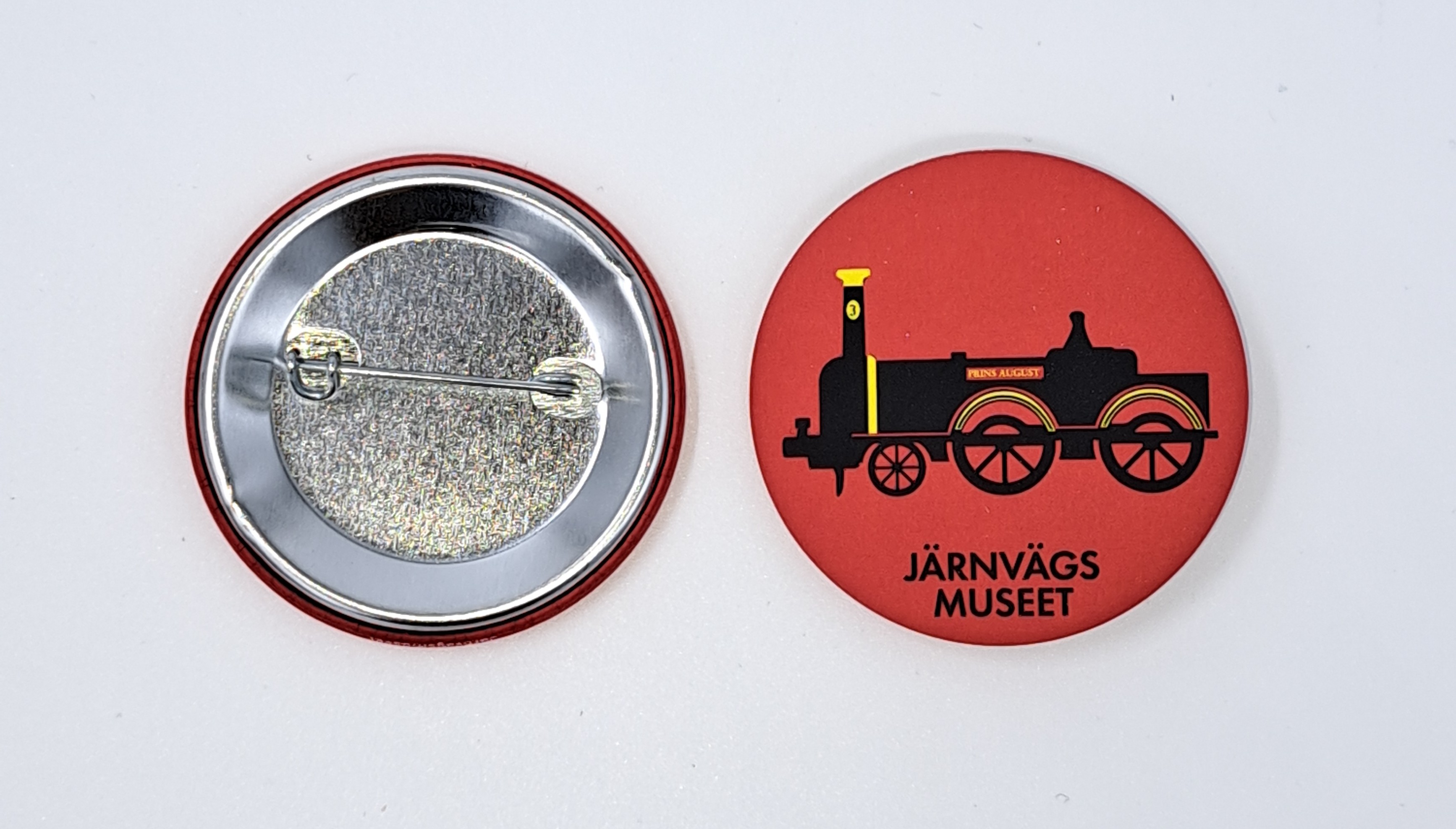 En rödorange pin med ett svart gammalt ånglok samt texten Järnvägsmuseet.