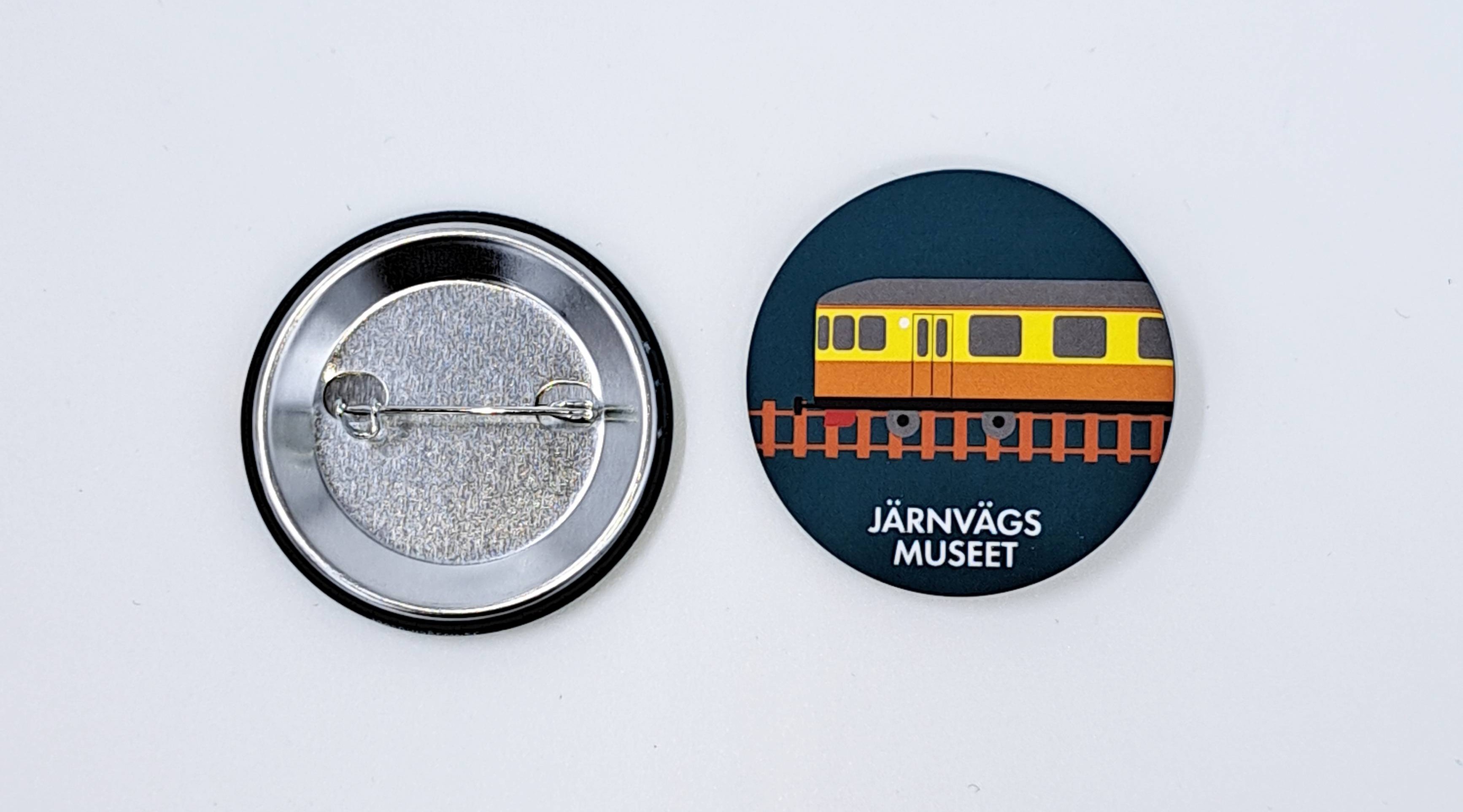 Skogsgrön pin med en gulorange rälsbuss som motiv och texten Järnvägsmuseet.