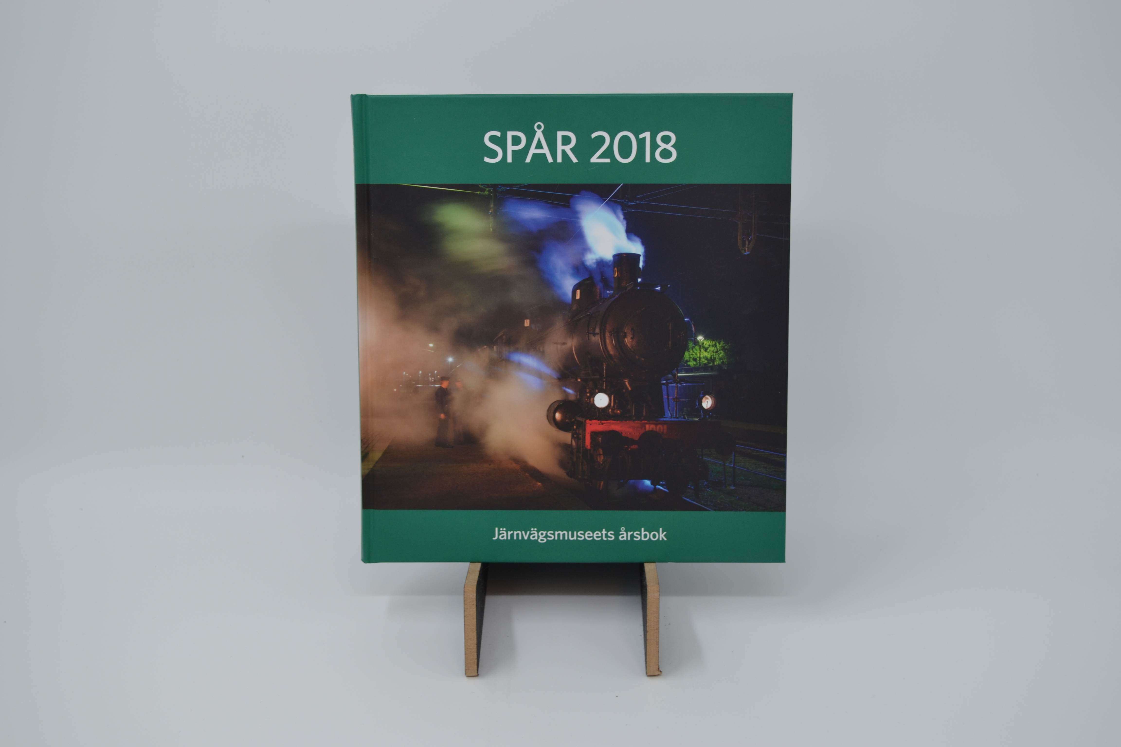 Ett svart ånglok i full fart på framsidan av boken "Spår 2018". 