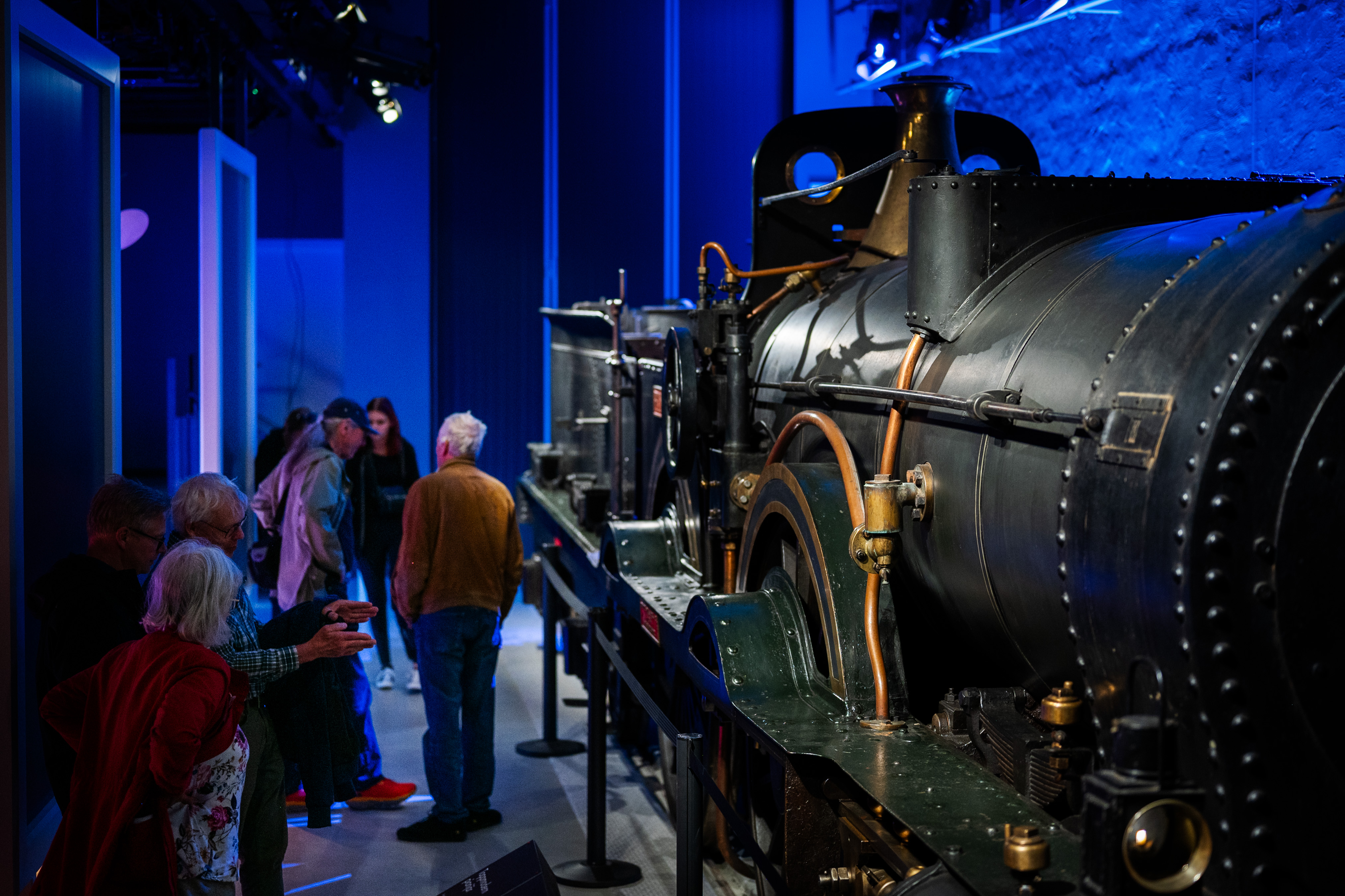 A group of people are standing in front of a big  steam locomotive in a exhibition hall