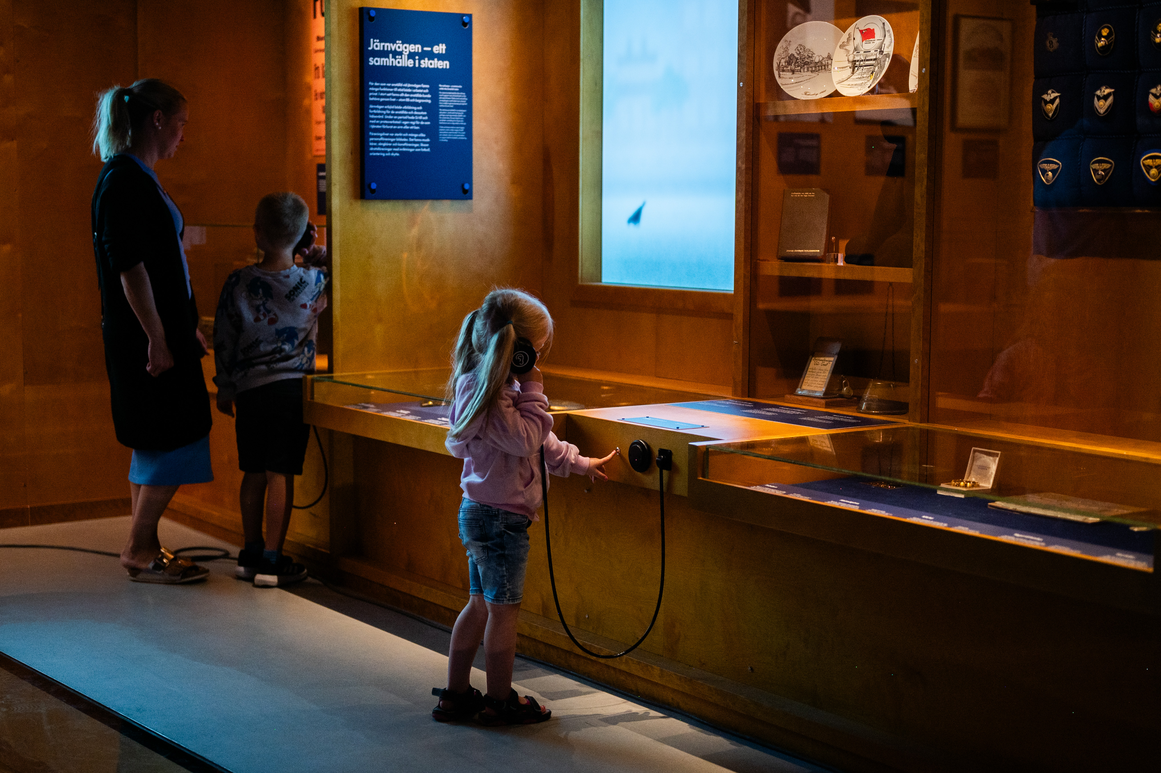 A girl is standning in front of a exhibition and listening to an audio track.