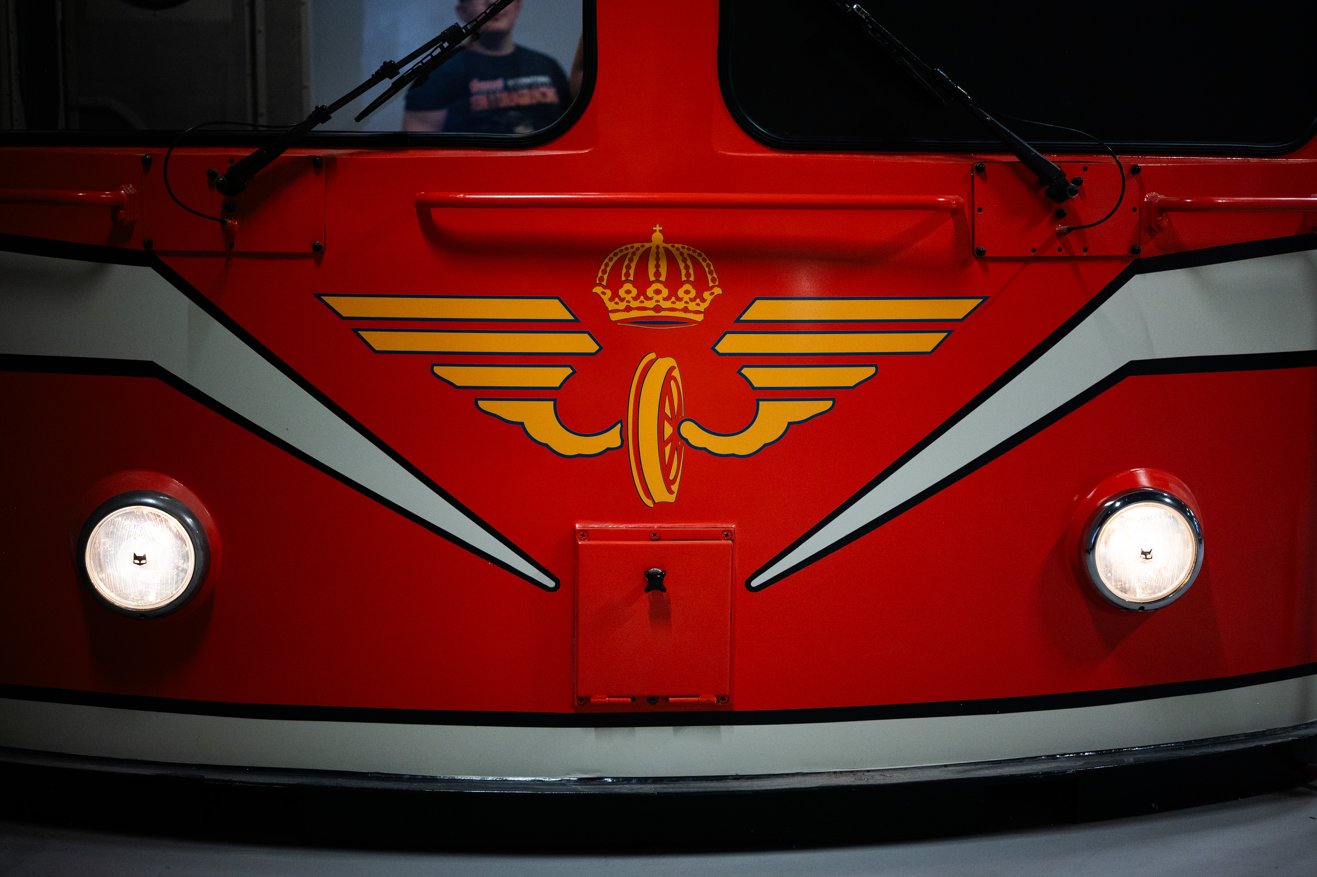 Close up of the front of a red train car with white details. Big glowing lights are on each side of the front.