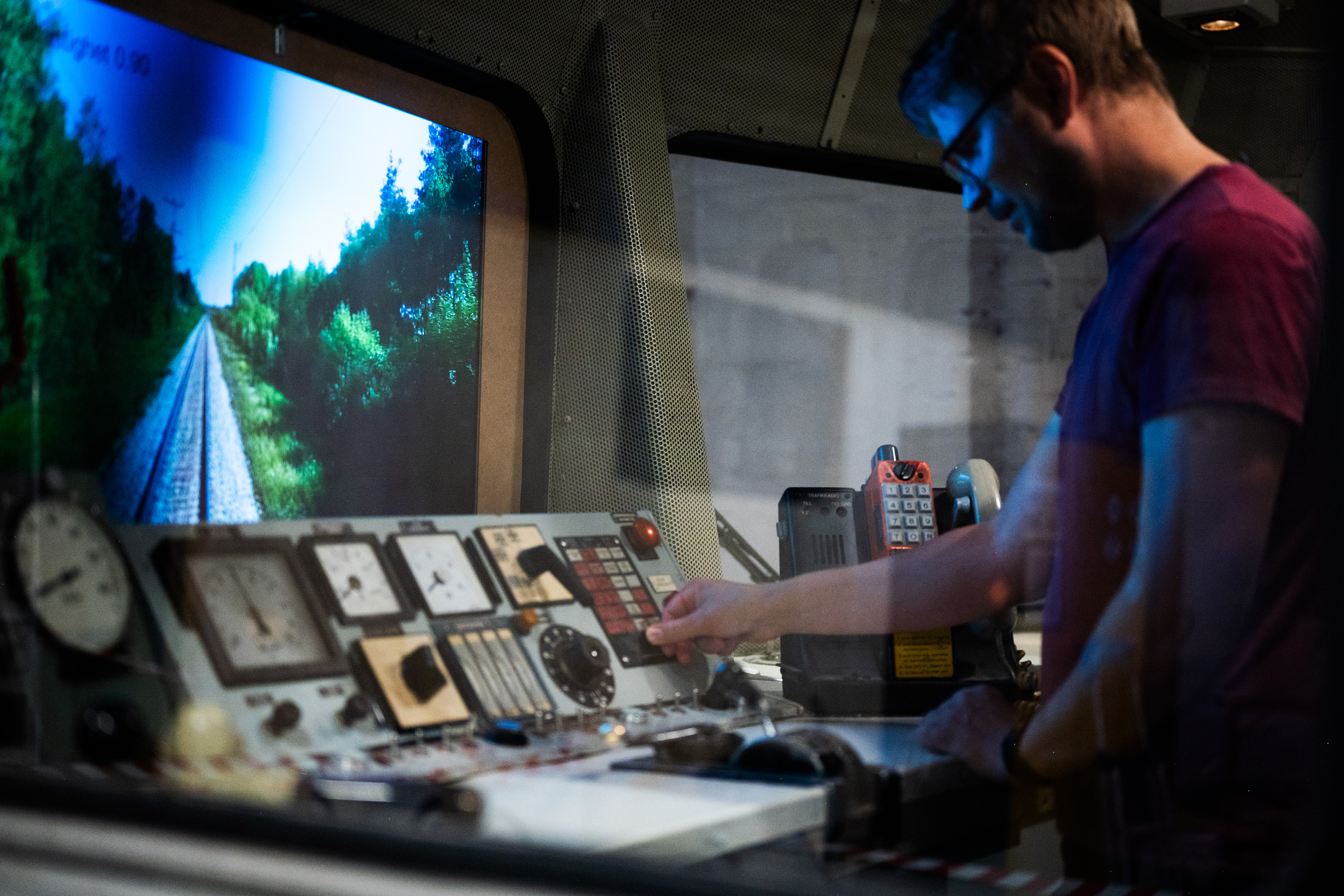 A man is standing in the drivers place in a train car and looking at a screen with a railroad on it.