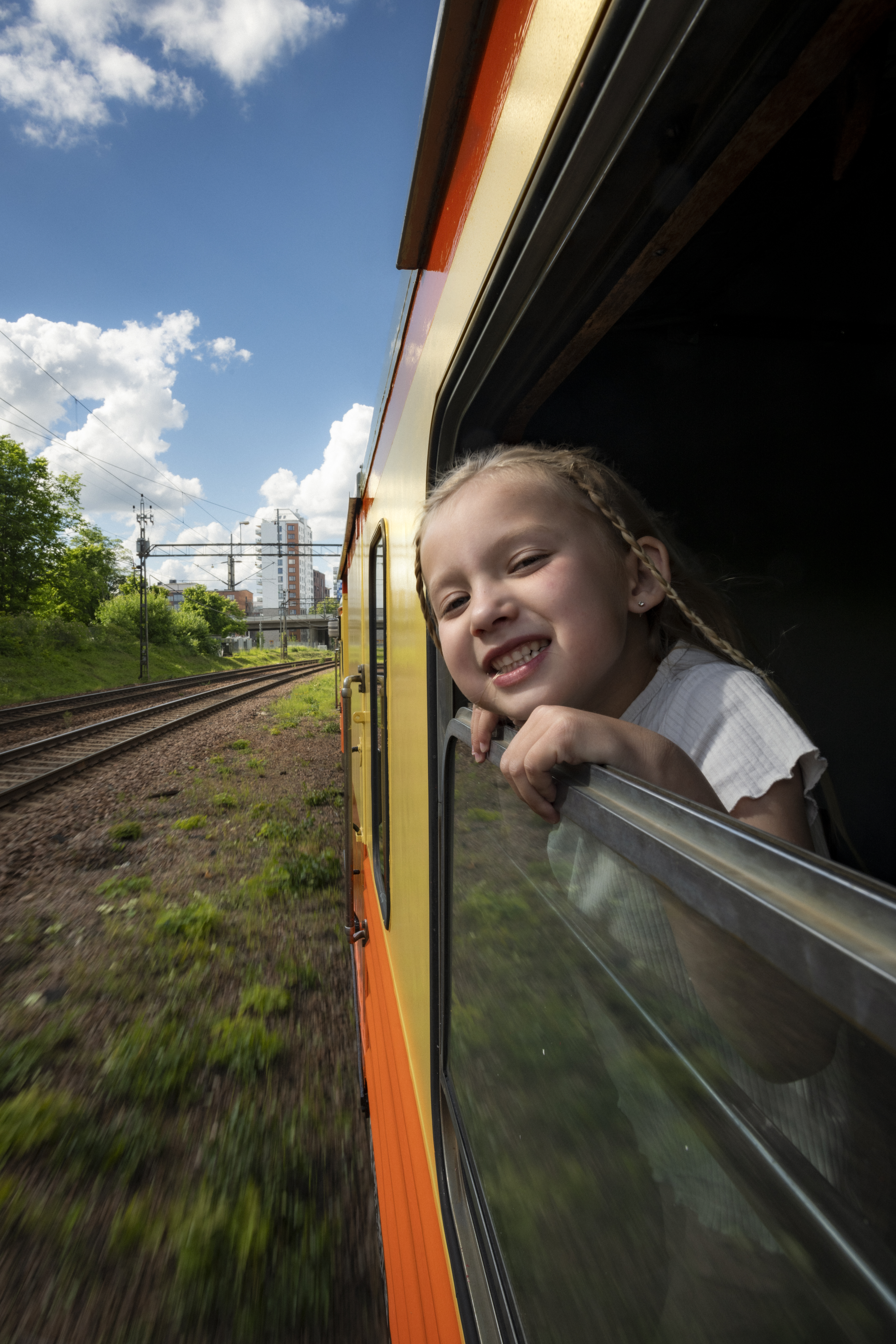 A smiling girl is lookig out of an open window on board a railcar