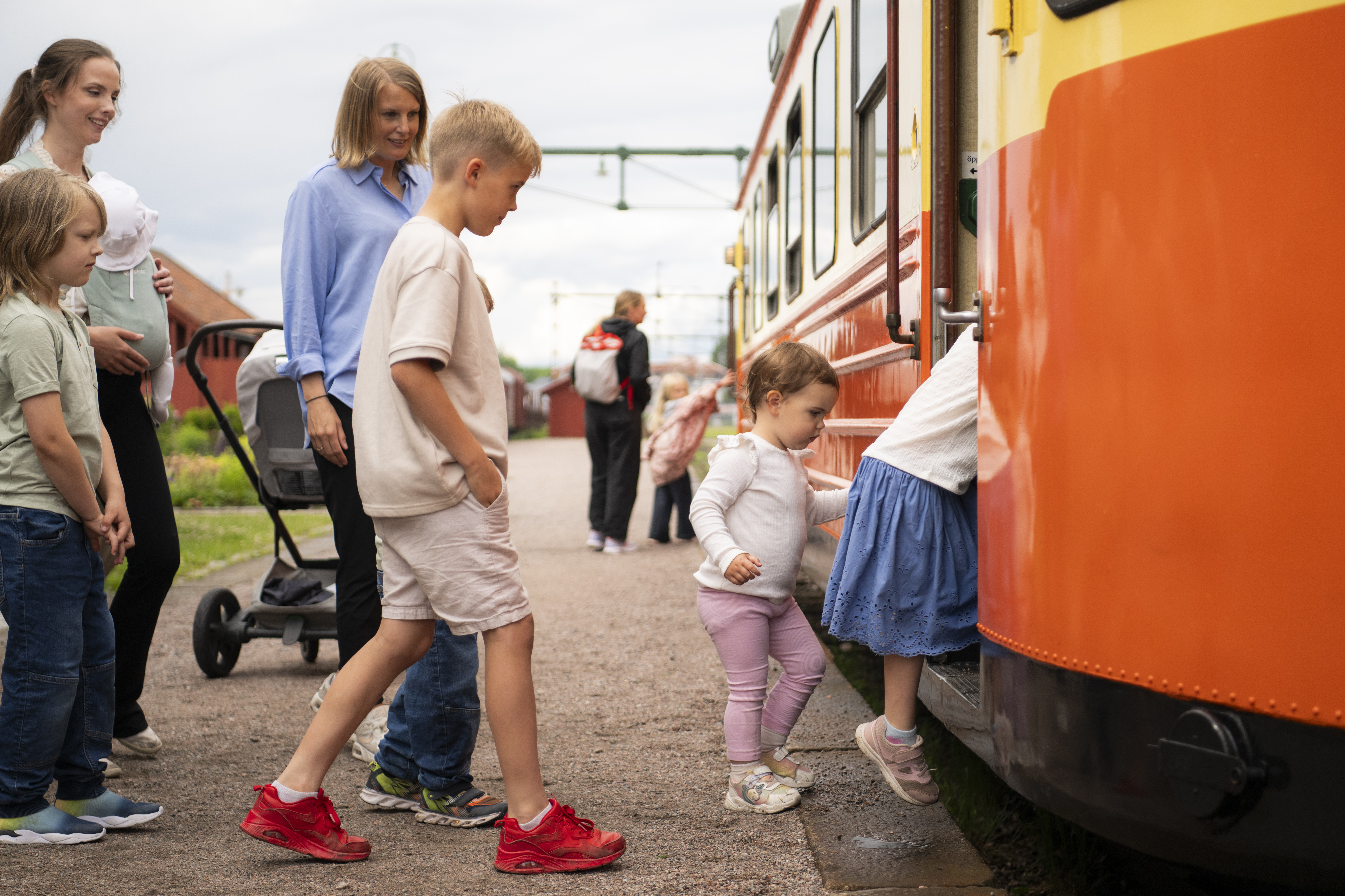 Barn och vuxna kliver på den orangea rälsbussen.