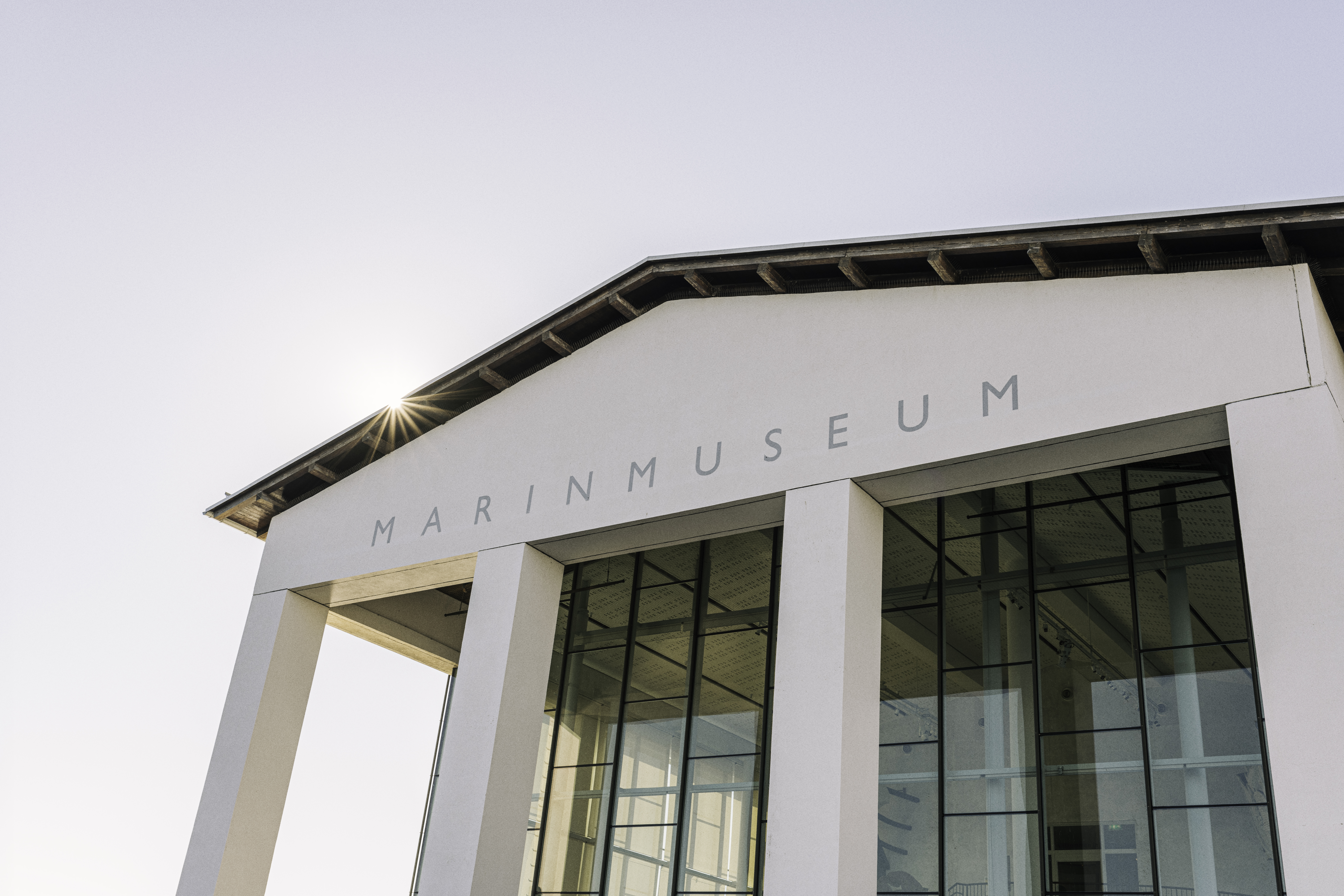 The Naval Museum's stately white façade with a sun glimpsed behind the roof.