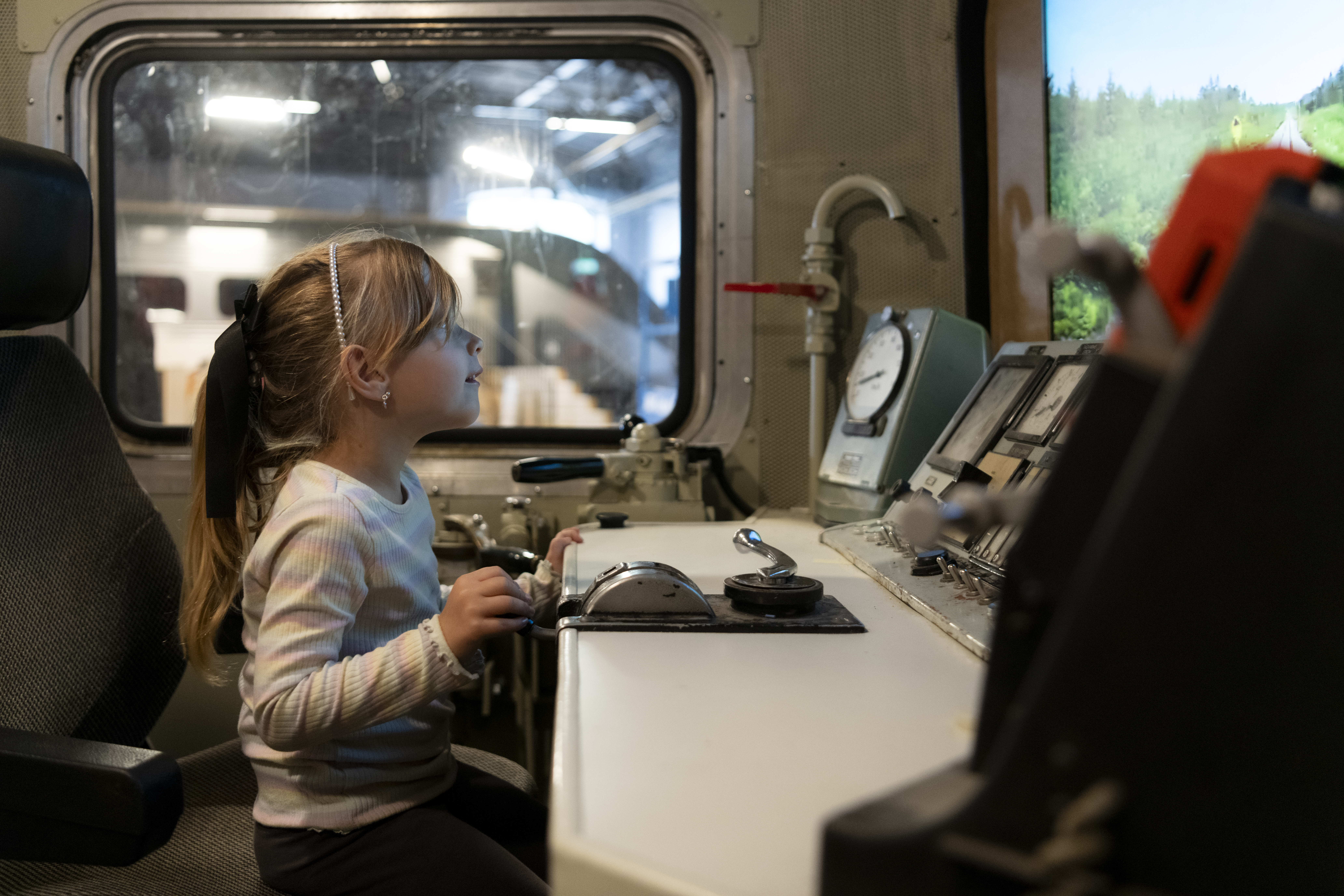 A girl is sitting in the drivers place in a train car