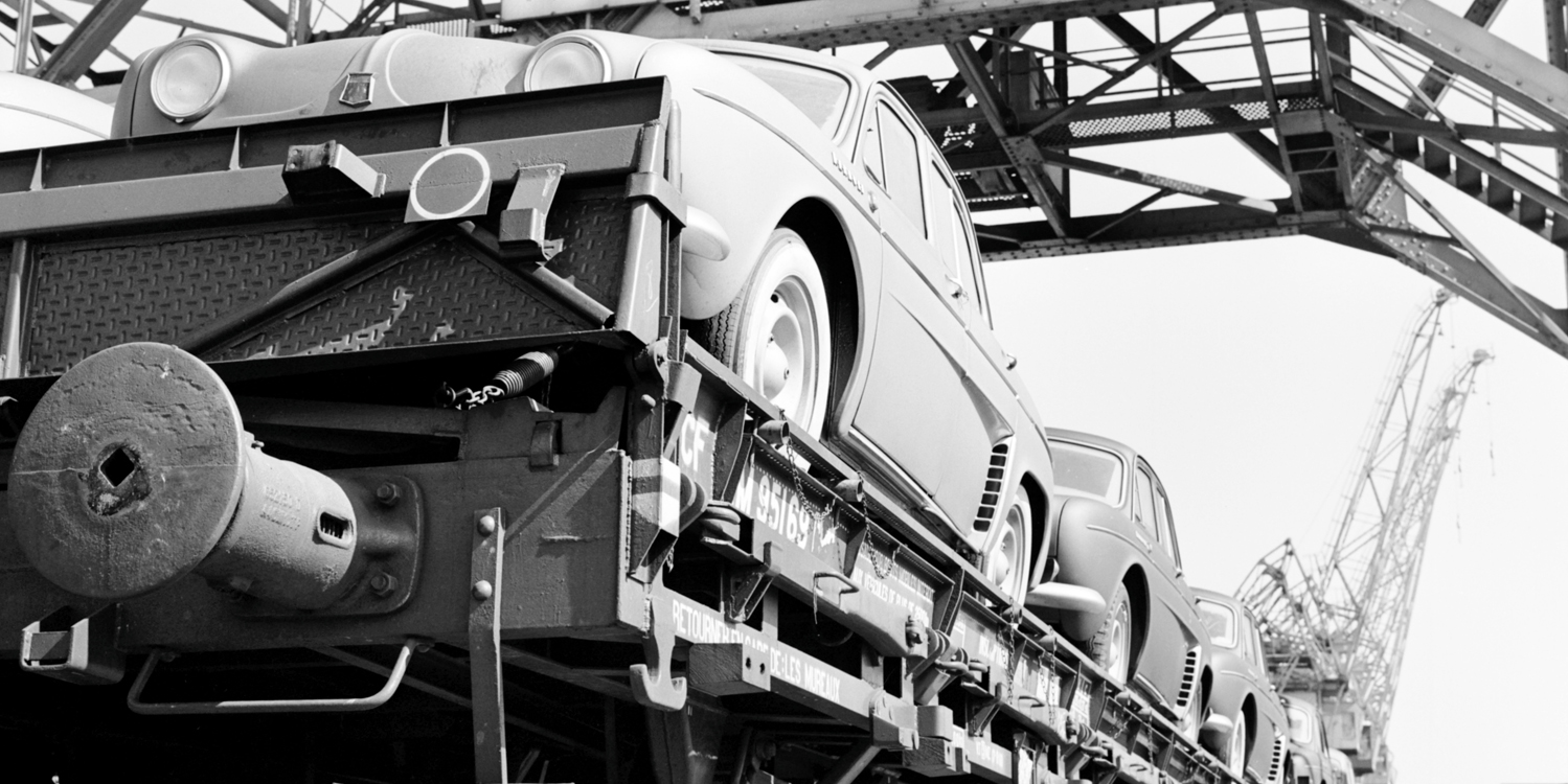 Närbild av öppen tågvagn där personbilar är lastade.