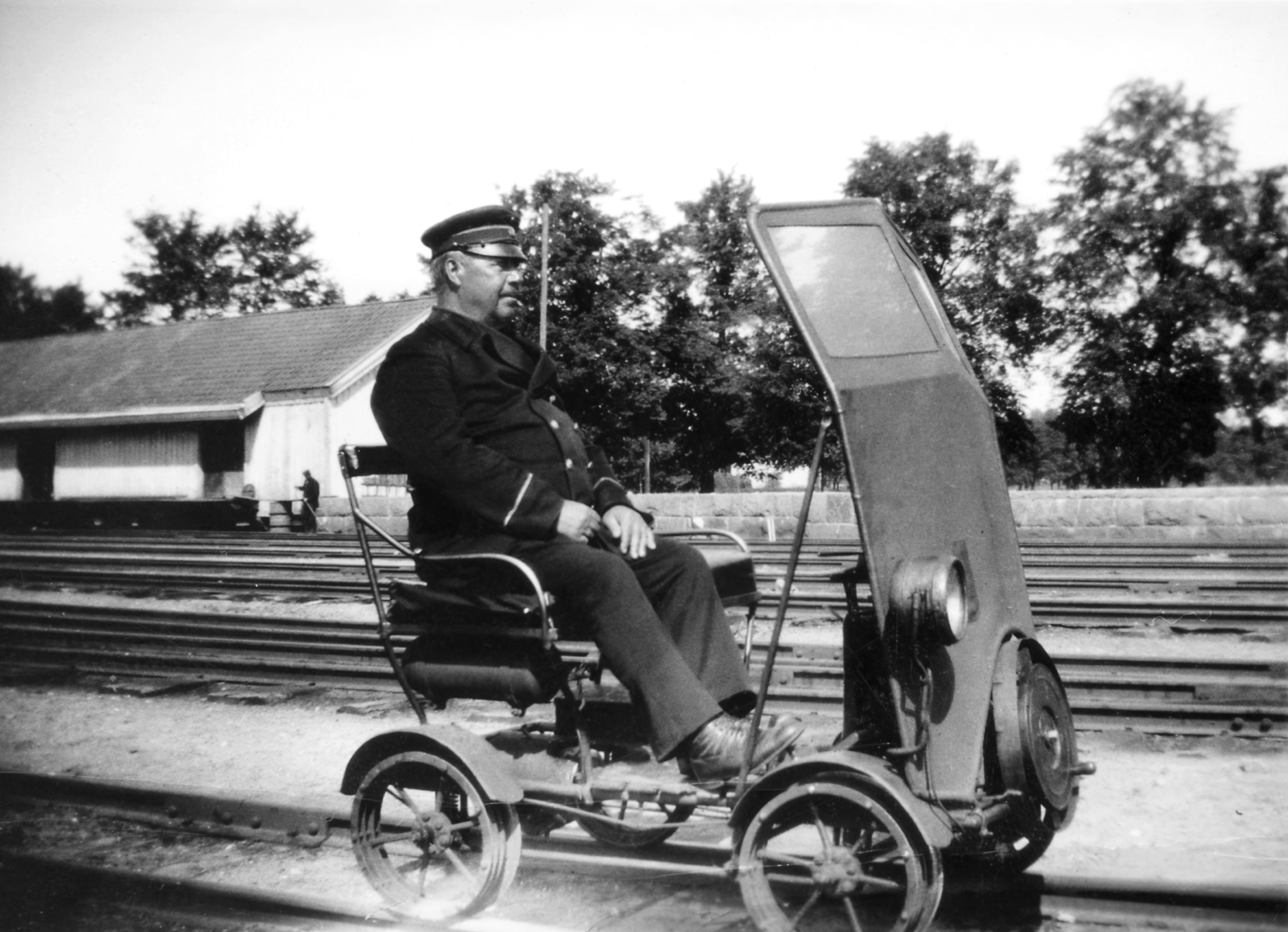 Uniformerad man sittandes på dressin med vindskydd på järnvägsspår.