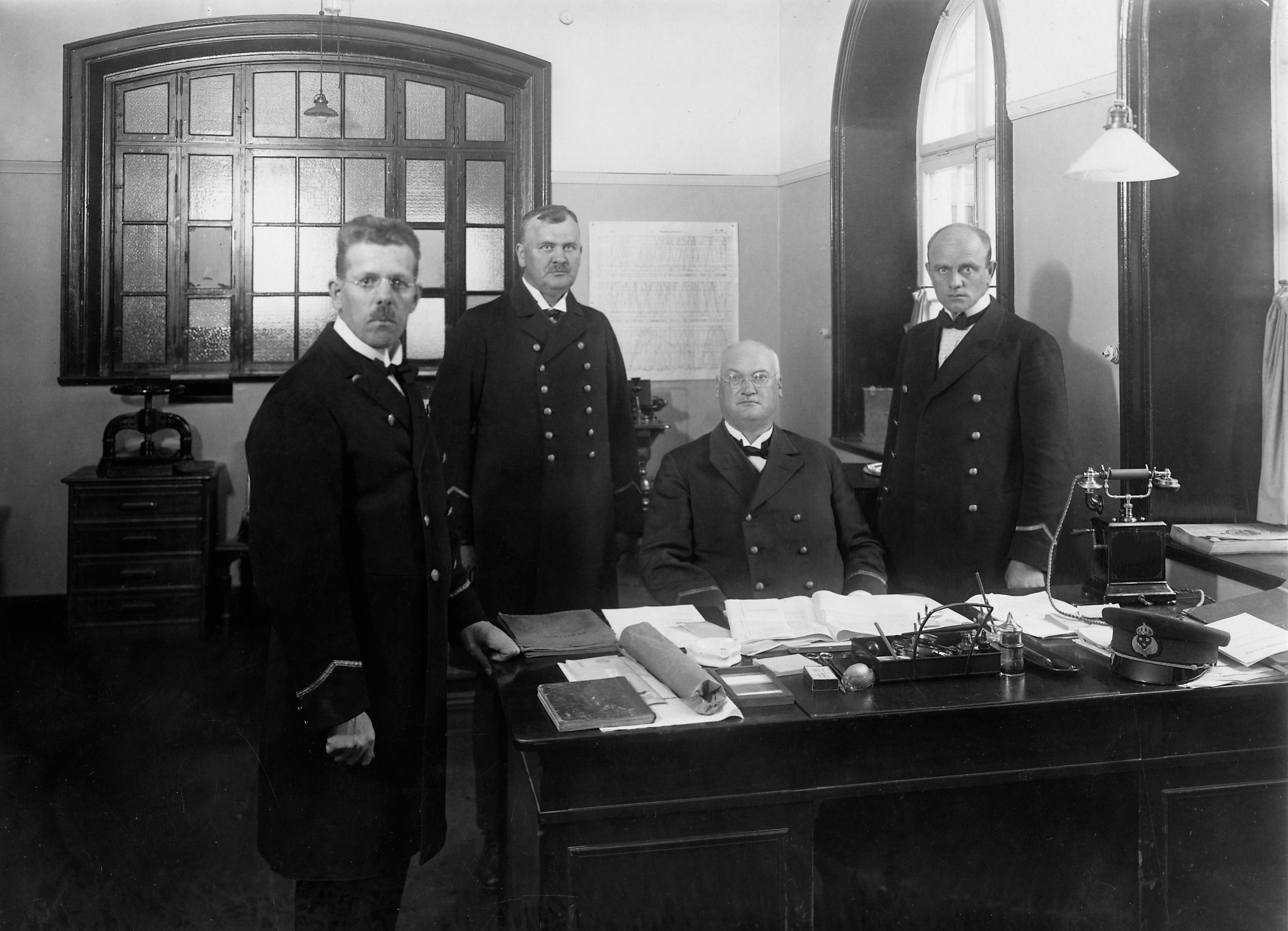 Four men gathered around a desk in an office environment.