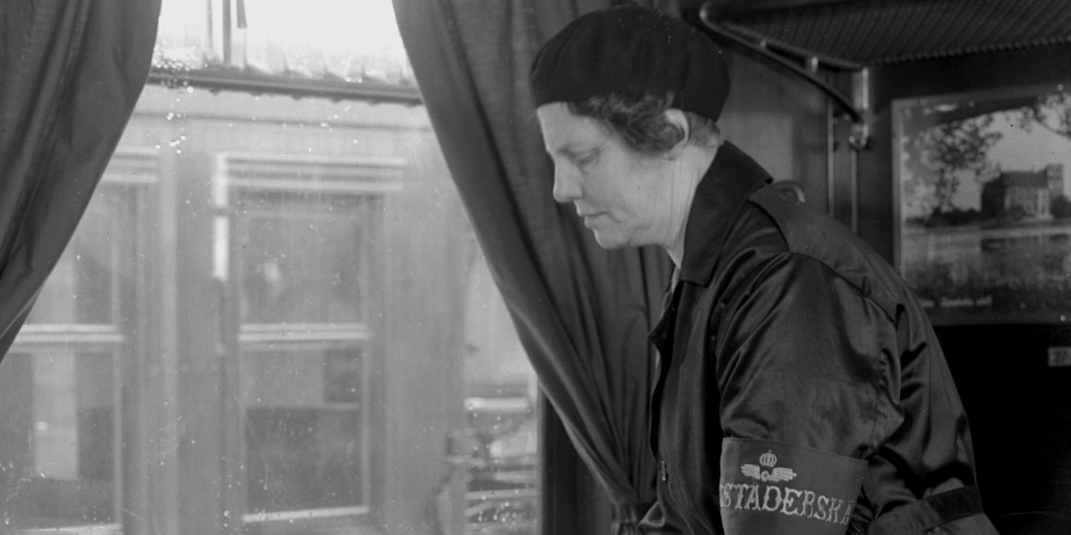 Woman wiping table in front of seated man in train compartment.