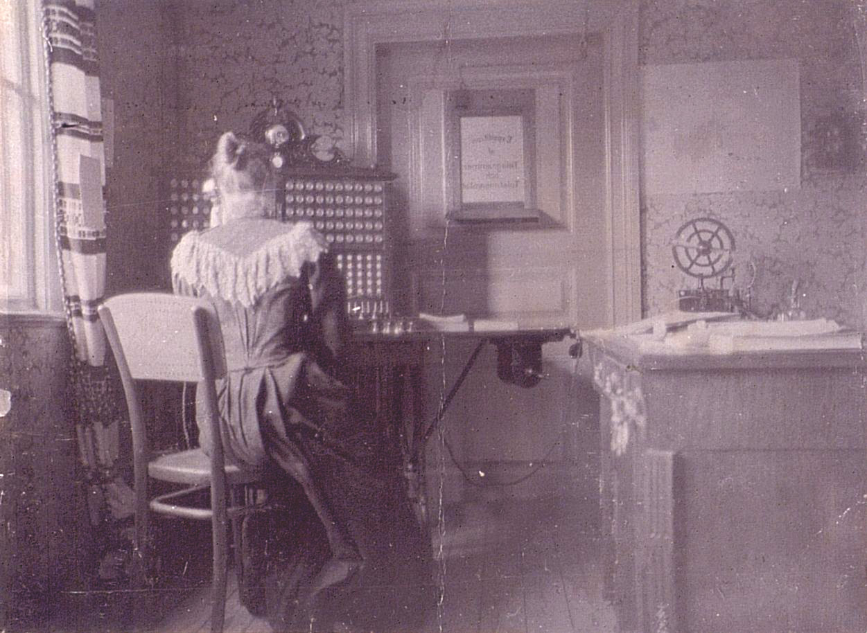 A woman sitting at a desk with a telephone. Picture is from the year 1890.