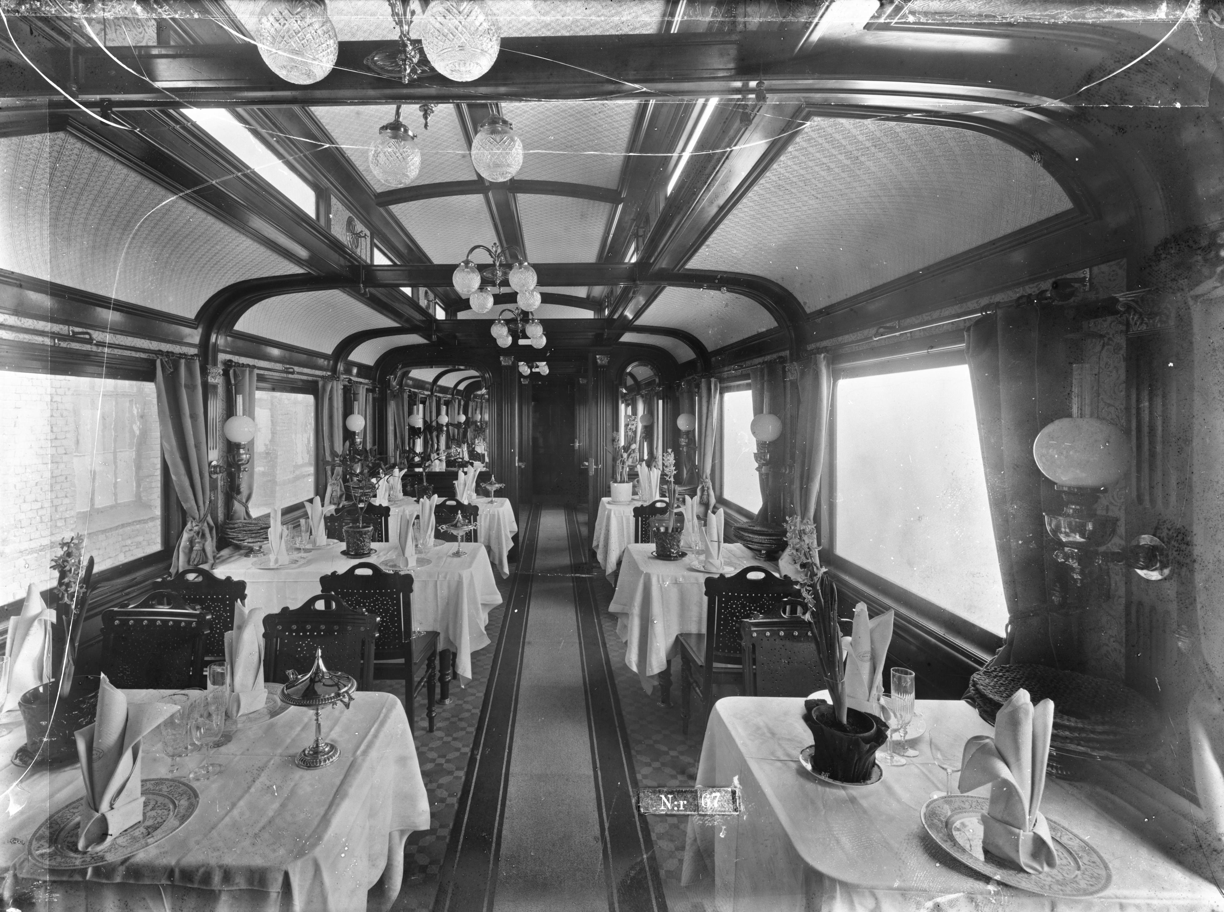Interior of an older restaurant trolley, tables set with white tablecloths and folded napkins. On each table is a pot of hyacinth.