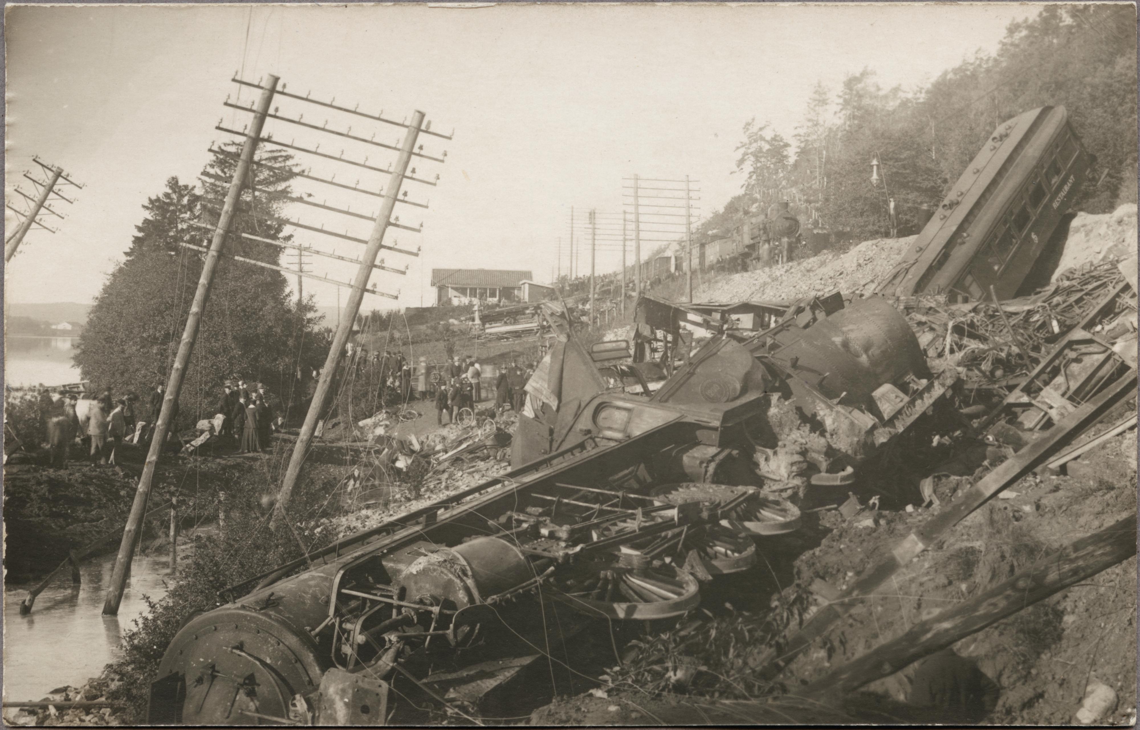 Demolished locomotives and carriages lie on their sides below the collapsed embankment.