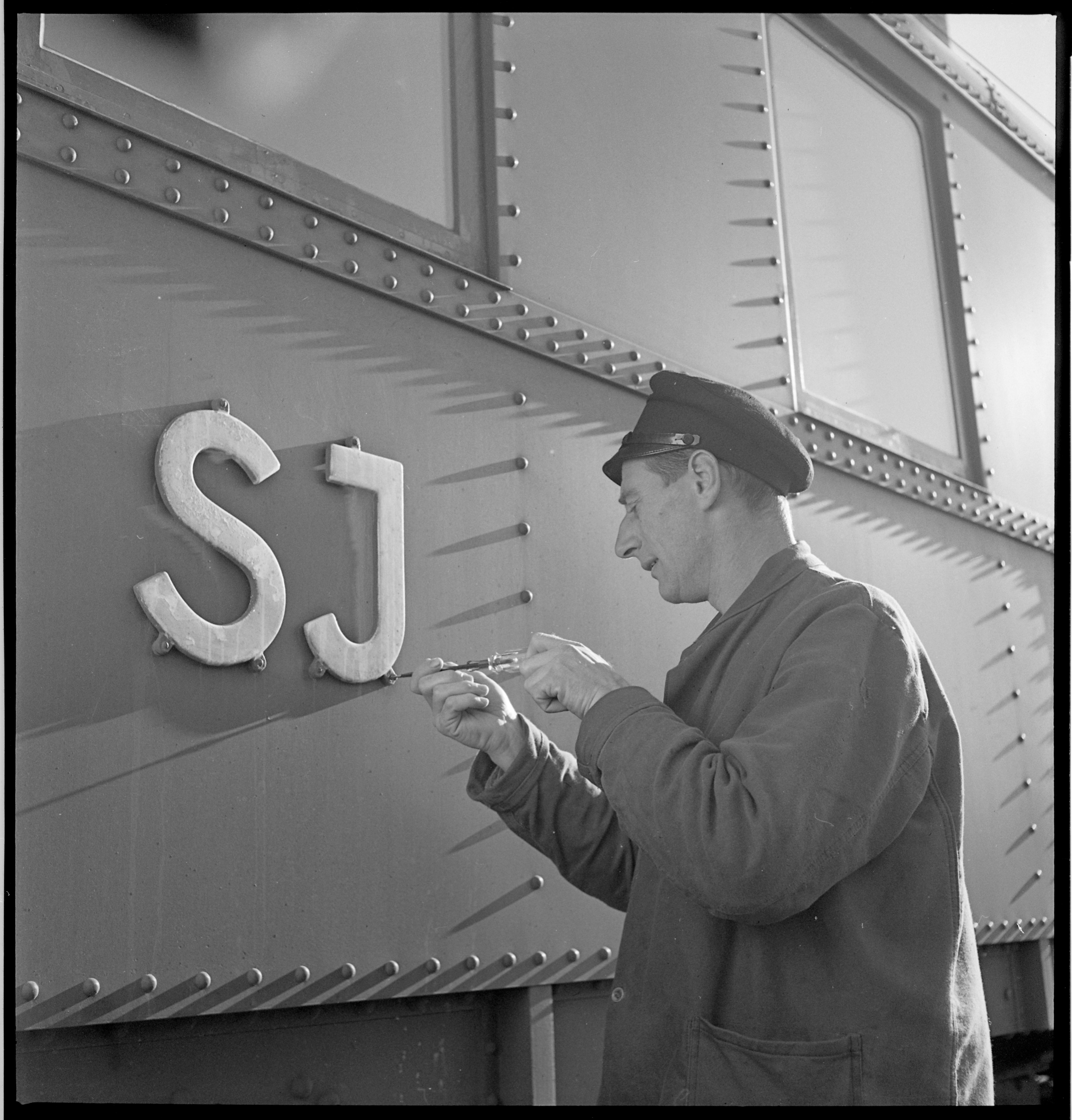 A man screws in a sign with SJ on the train carriage exterior.