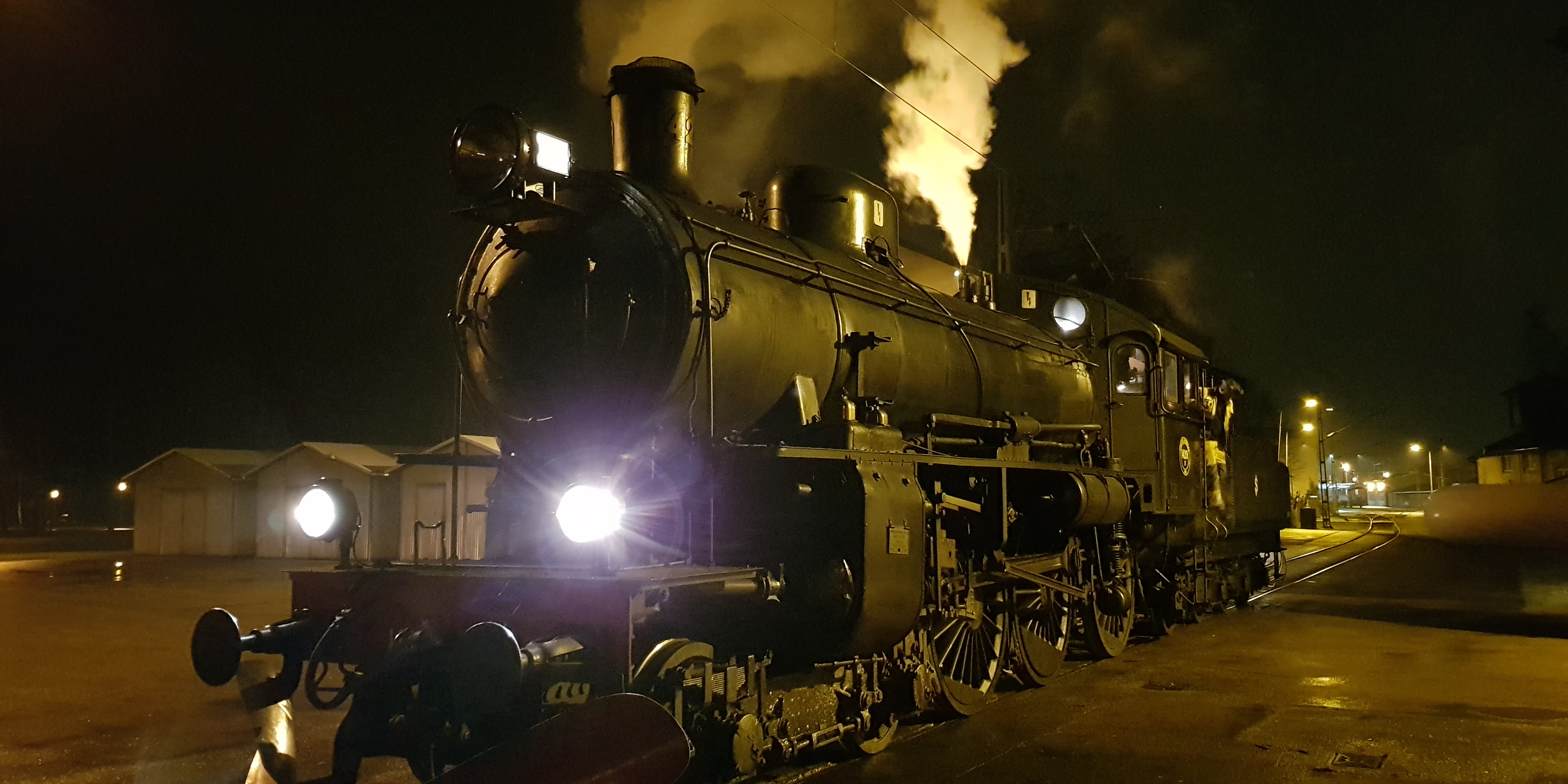 Dark evening picture of a rail with a luminous black steam locomotive puffing smoke.