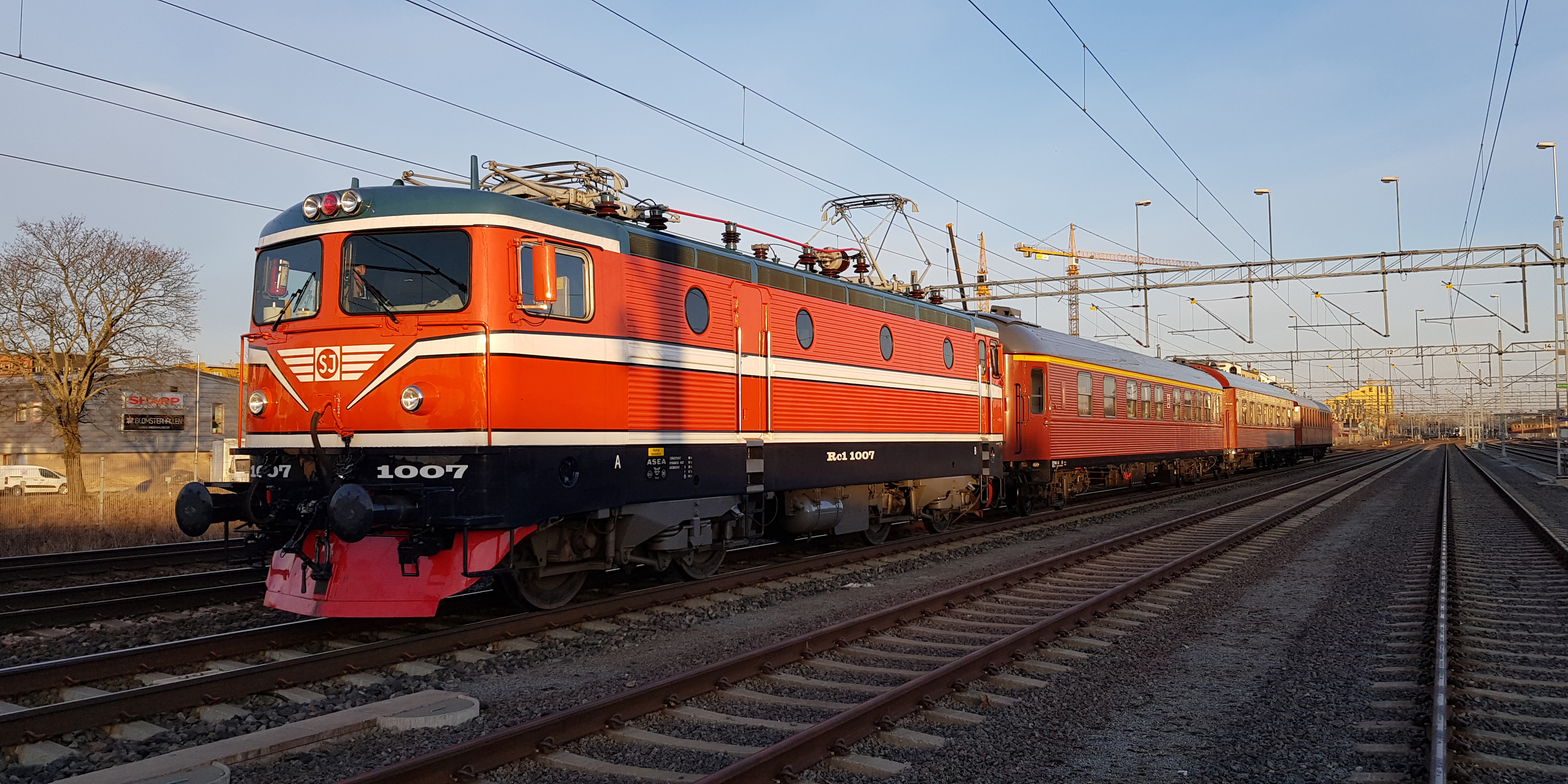 Orange lok med flera personvagnar på bangård med många spår. 