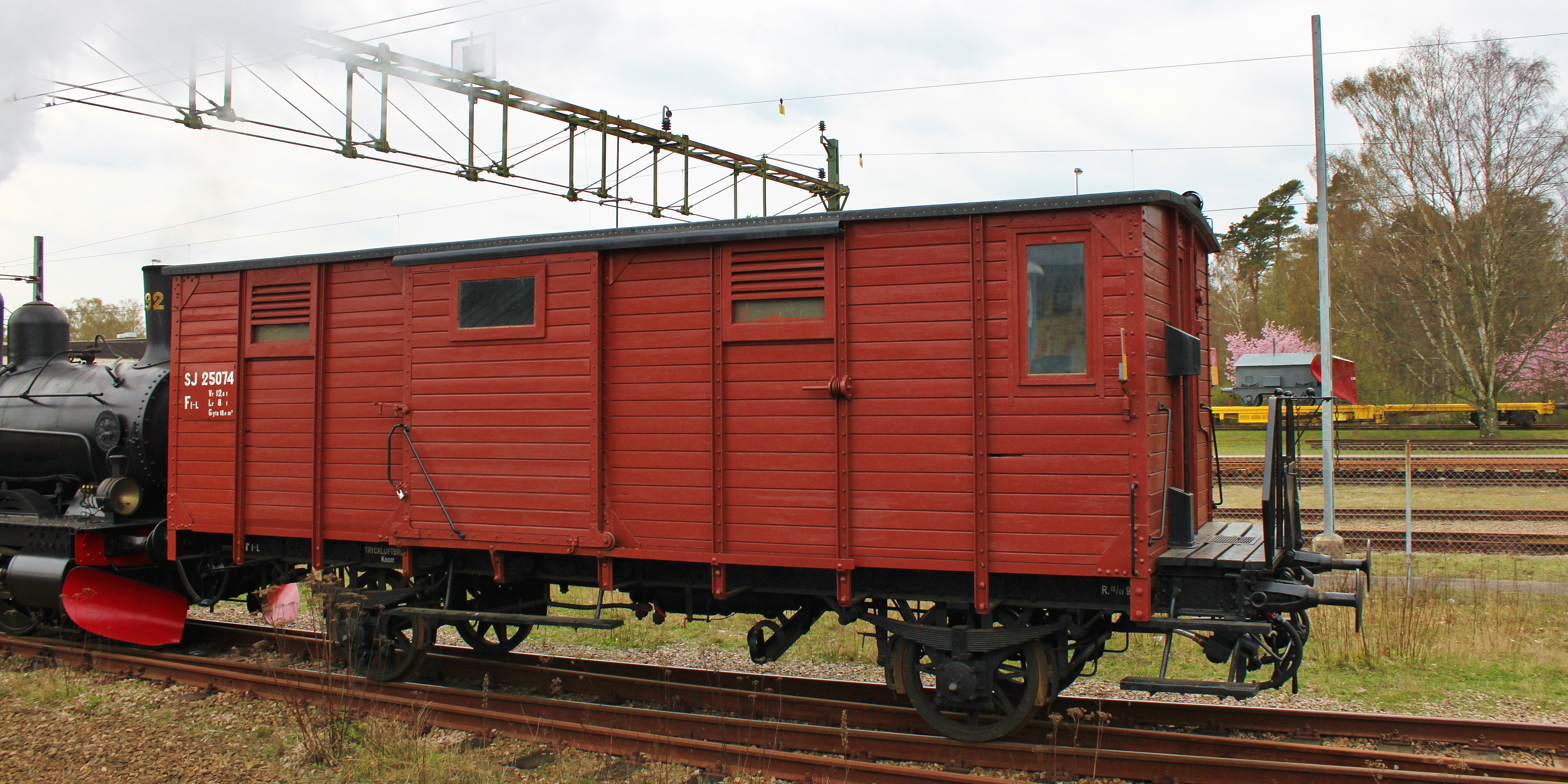 En gammal godsvagn i rödmålat trä från 1899 dras av ett svart ånglok.