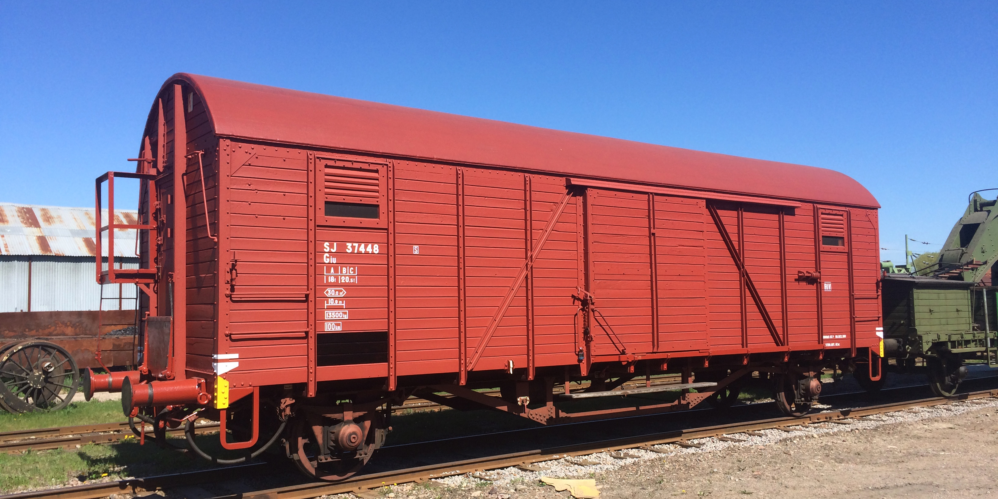 En klarröd rymlig godsvagn står stillastående på ett spår.