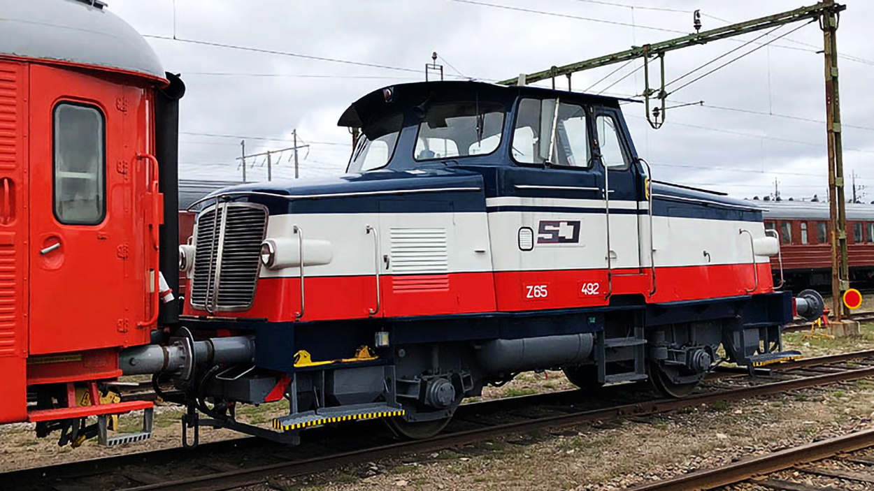 Smaller locomotives in blue, white and red coupled to dark red passenger car.