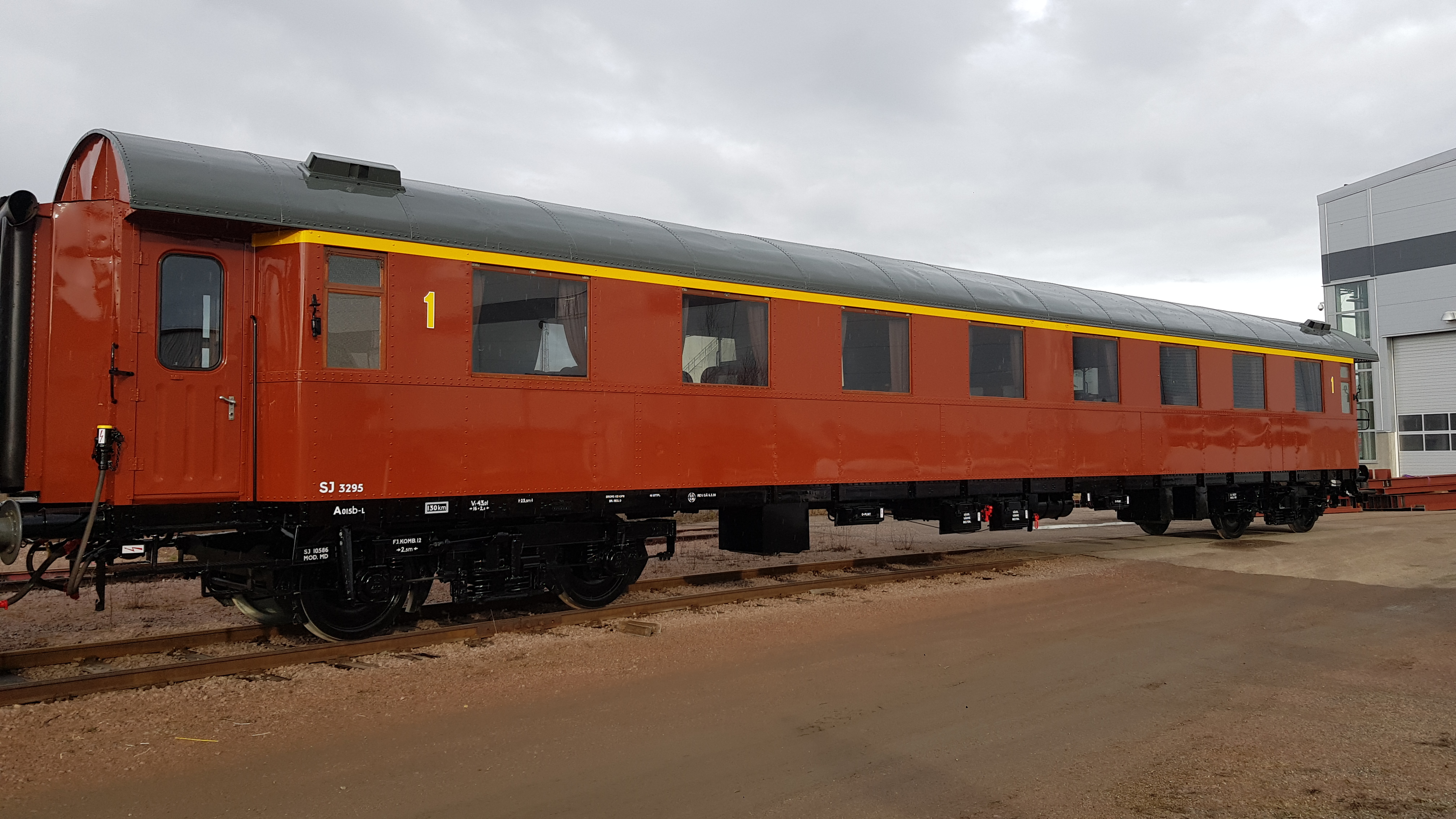 Roströd personvagn med gult streck ovanför fönstren placerad på spårområde.