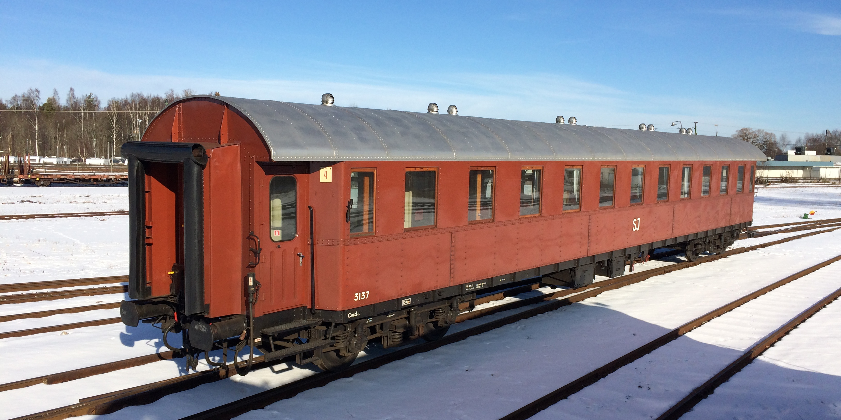 Roströd personvagn placerad på stationsområde.