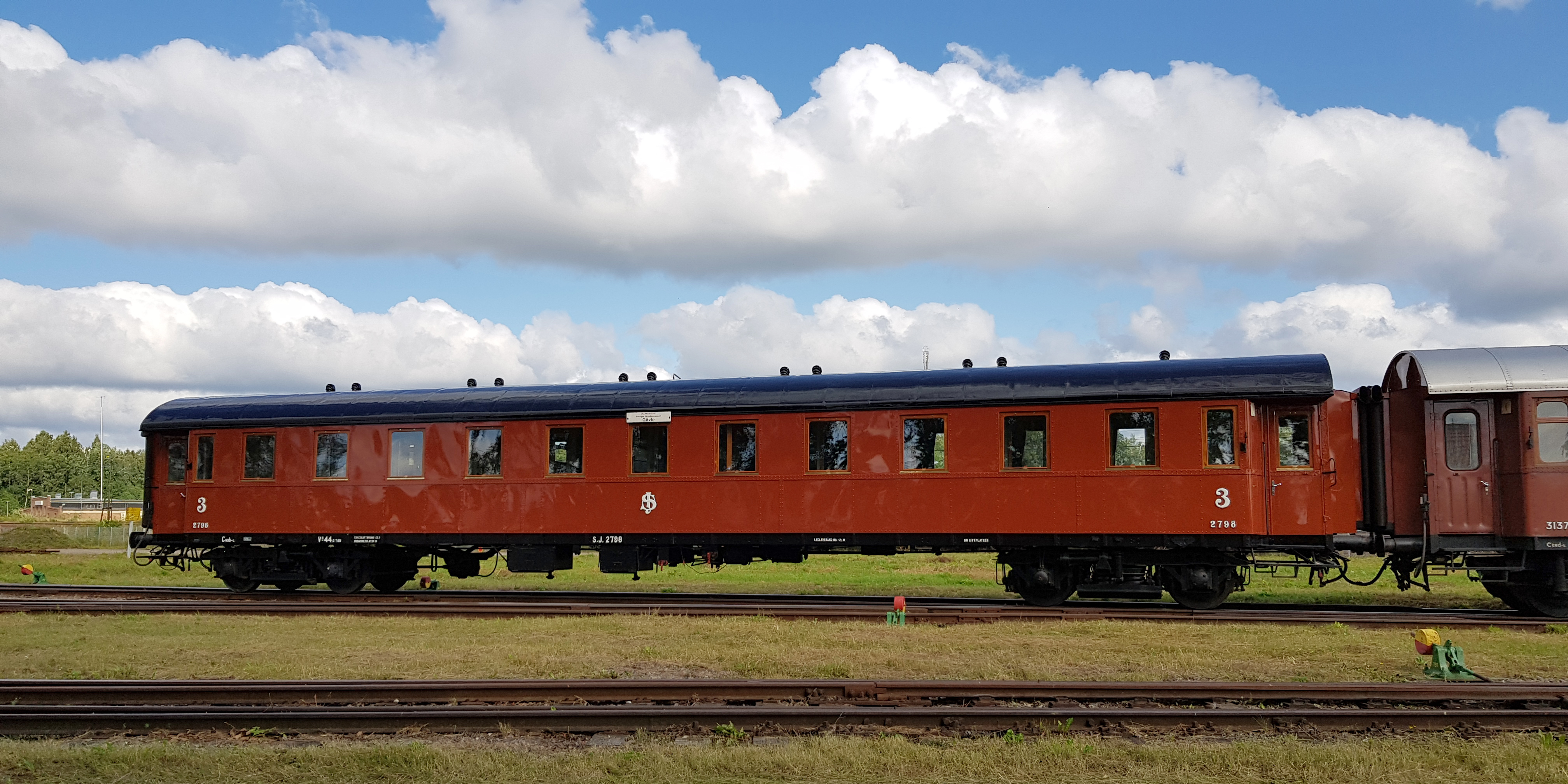 Roströd personvagn kopplad mellan andra vagnar.