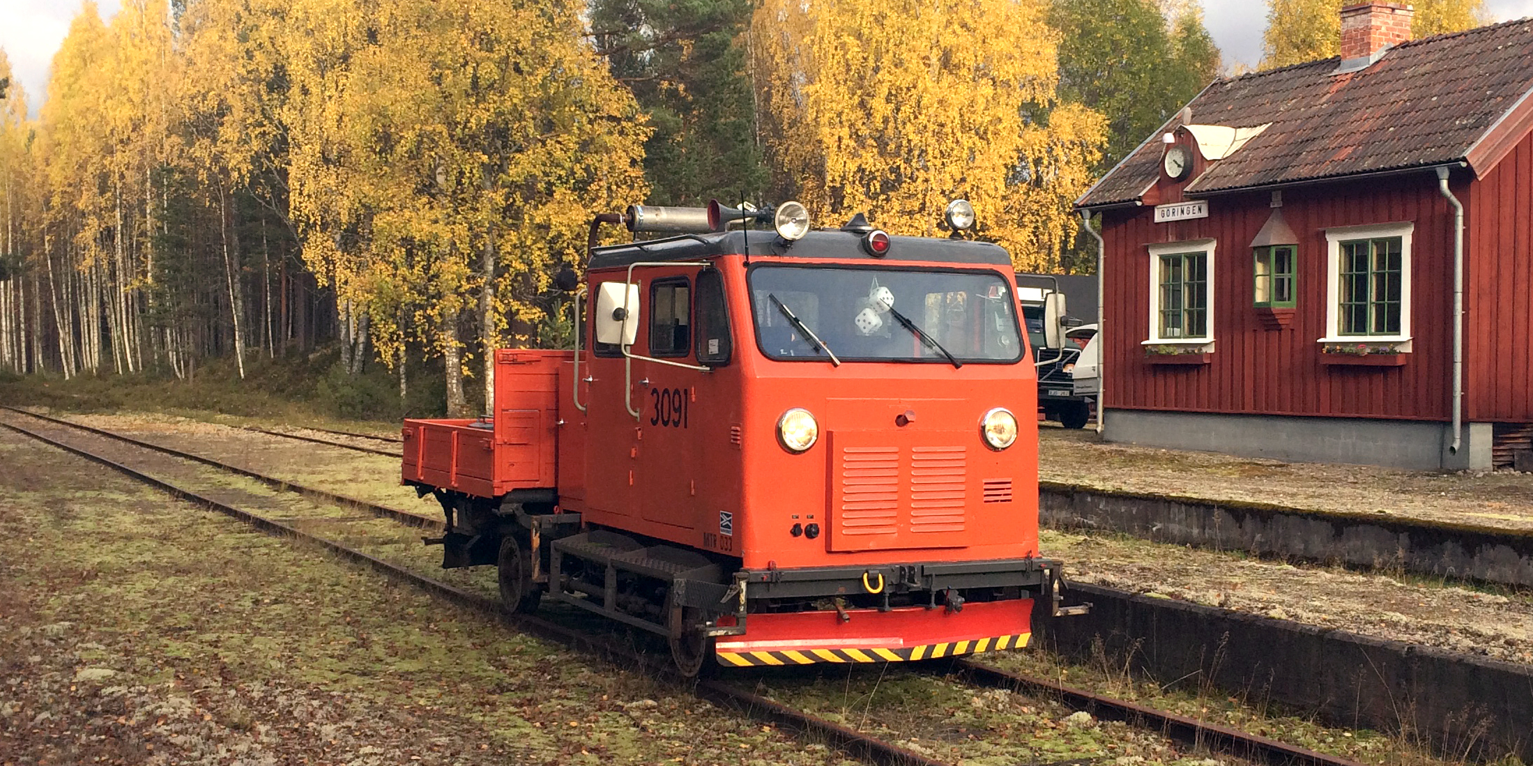 A small red locomotive (trolley) on rails in autumn landscape.