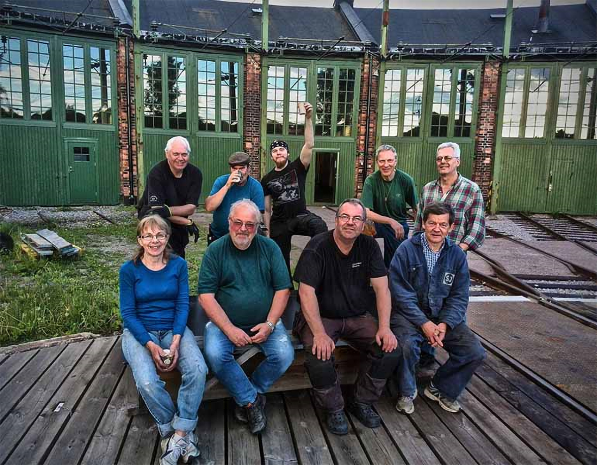 En gruppbild på entusiastiska vänföreningsmedlemmar framför ett grönt lokstall.